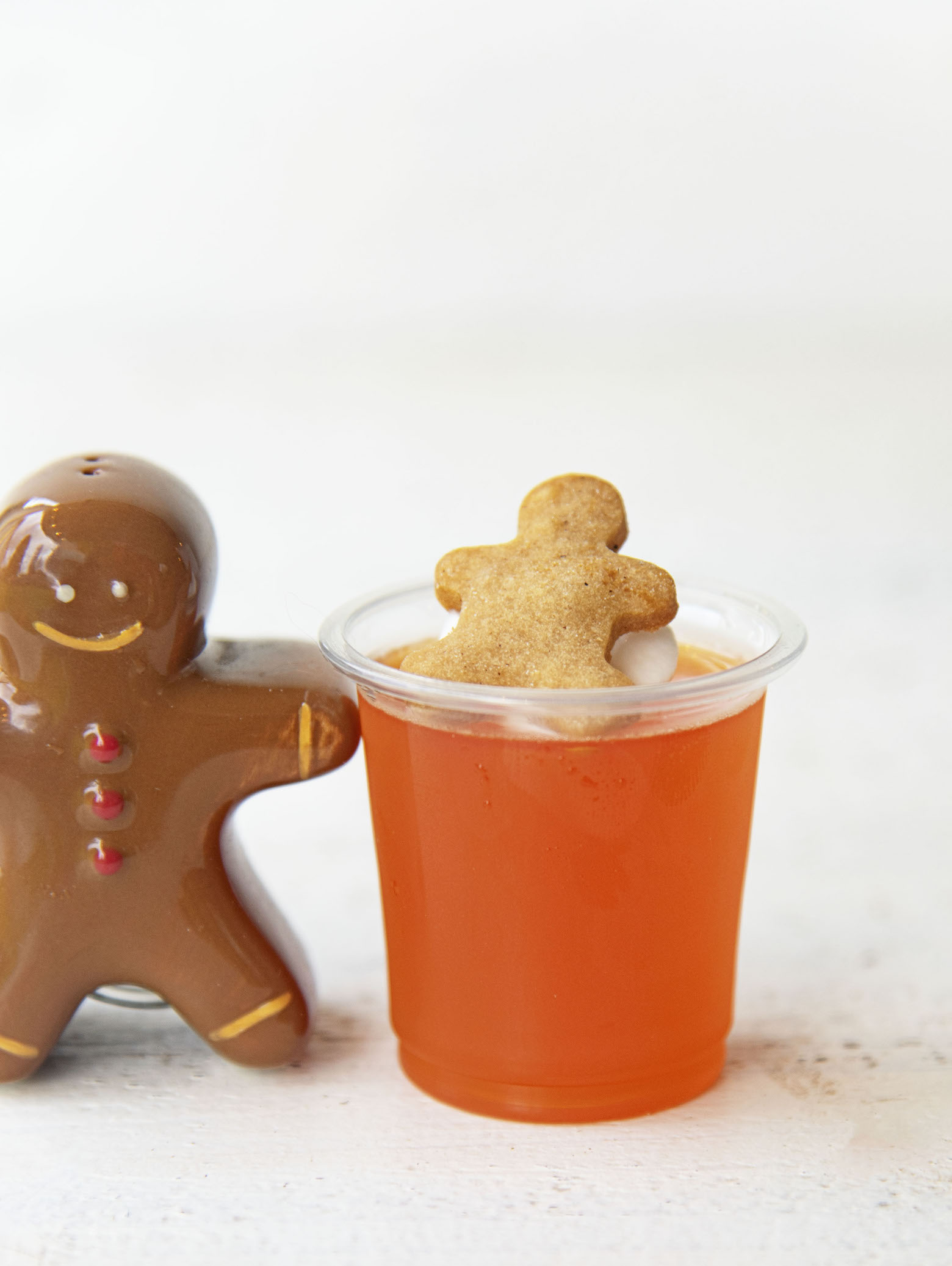 Side shot of single Orange Gingerbread Jello Shot with gingerbread man figurine at the side of the shot.