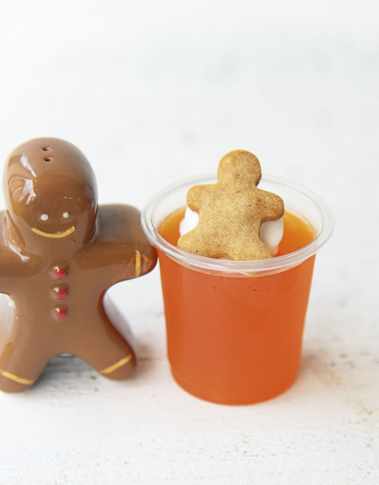 Single shot of Orange Gingerbread Jello Shot with gingerbread man figuring to the side of it. 