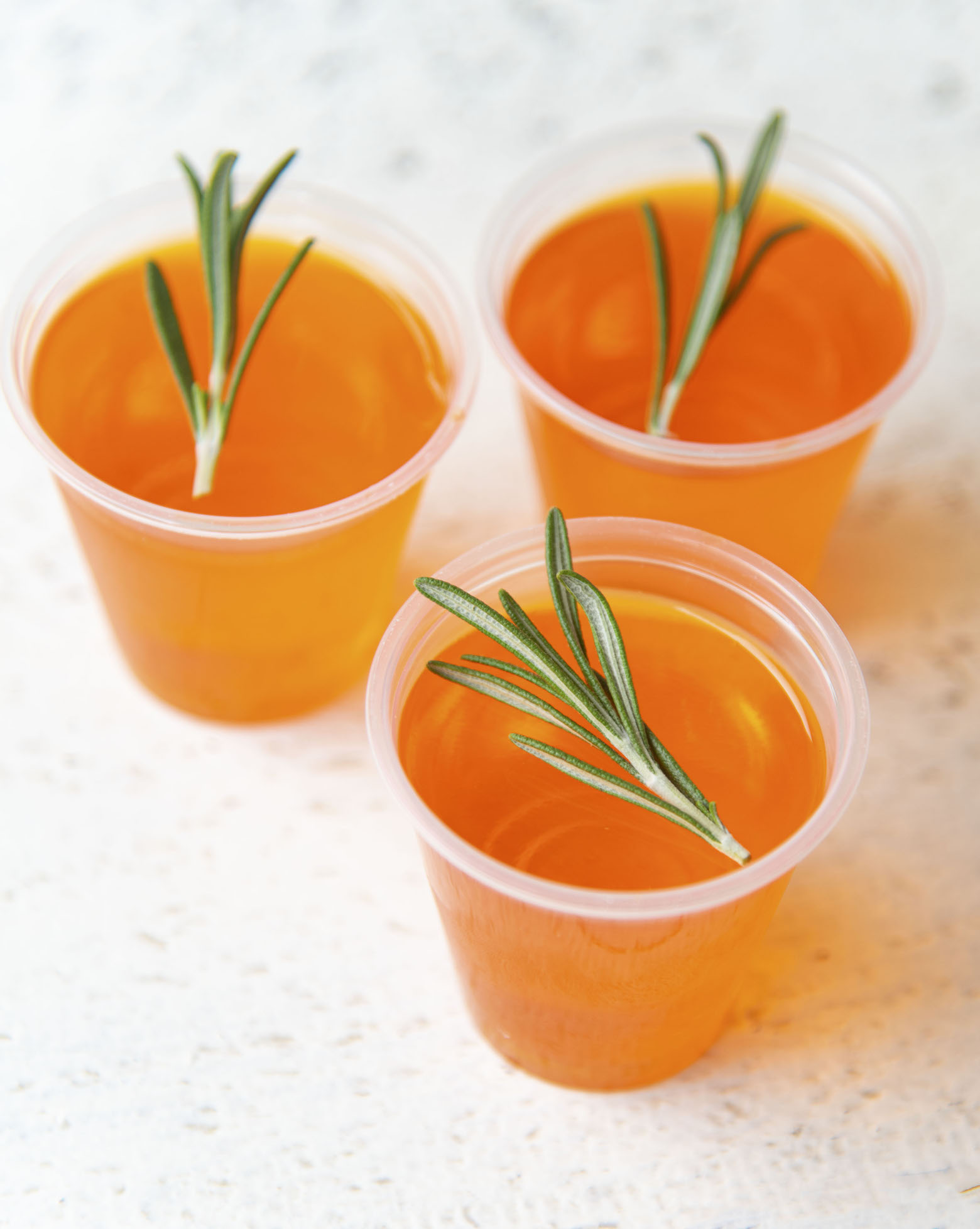 Three Winter Sun Jello Shots gathered with rosemary as garnish. 