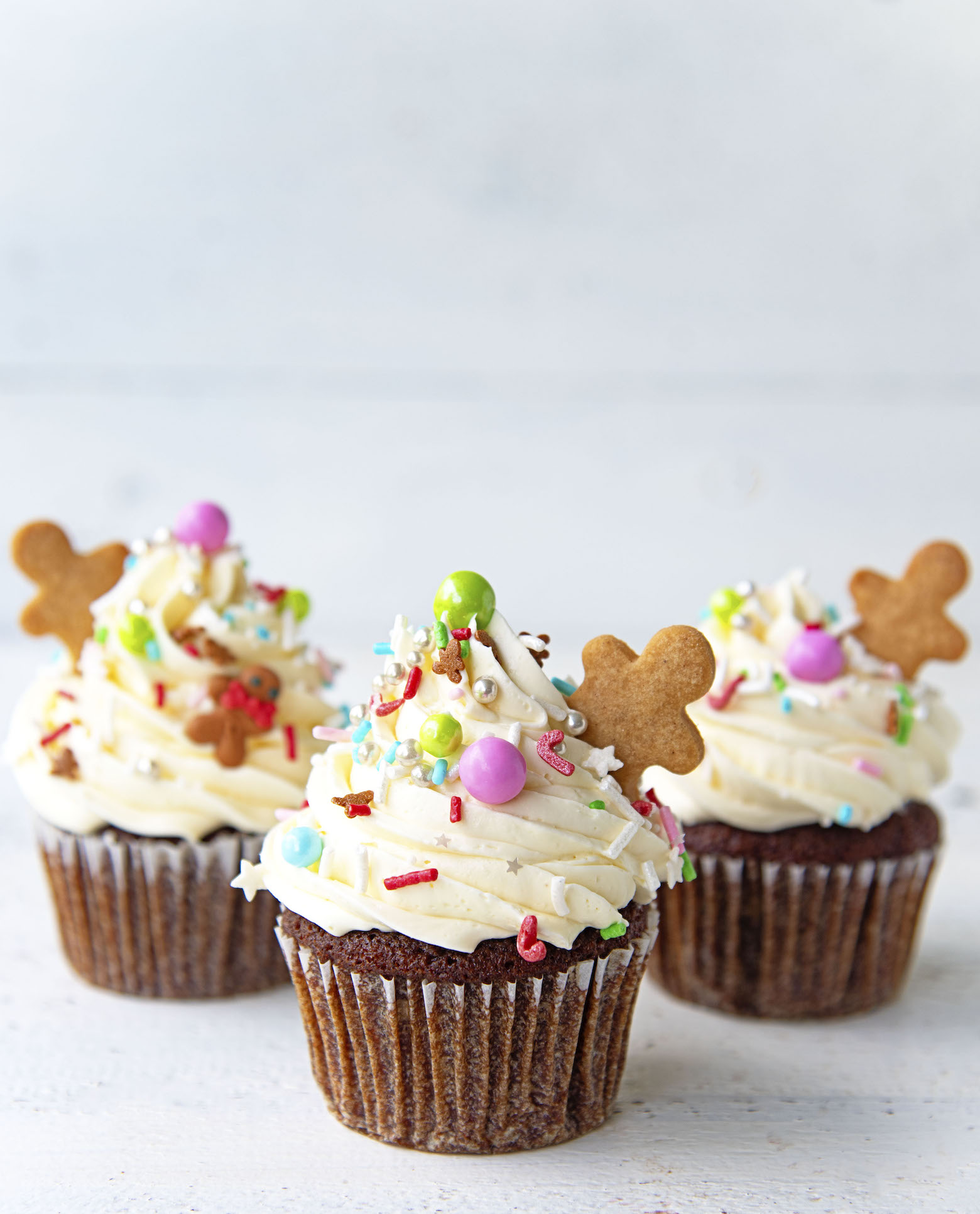 Side view of three Gingerbread White Chocolate Cupcakes with the gingerbread cookie men sticking out of the frosting. 