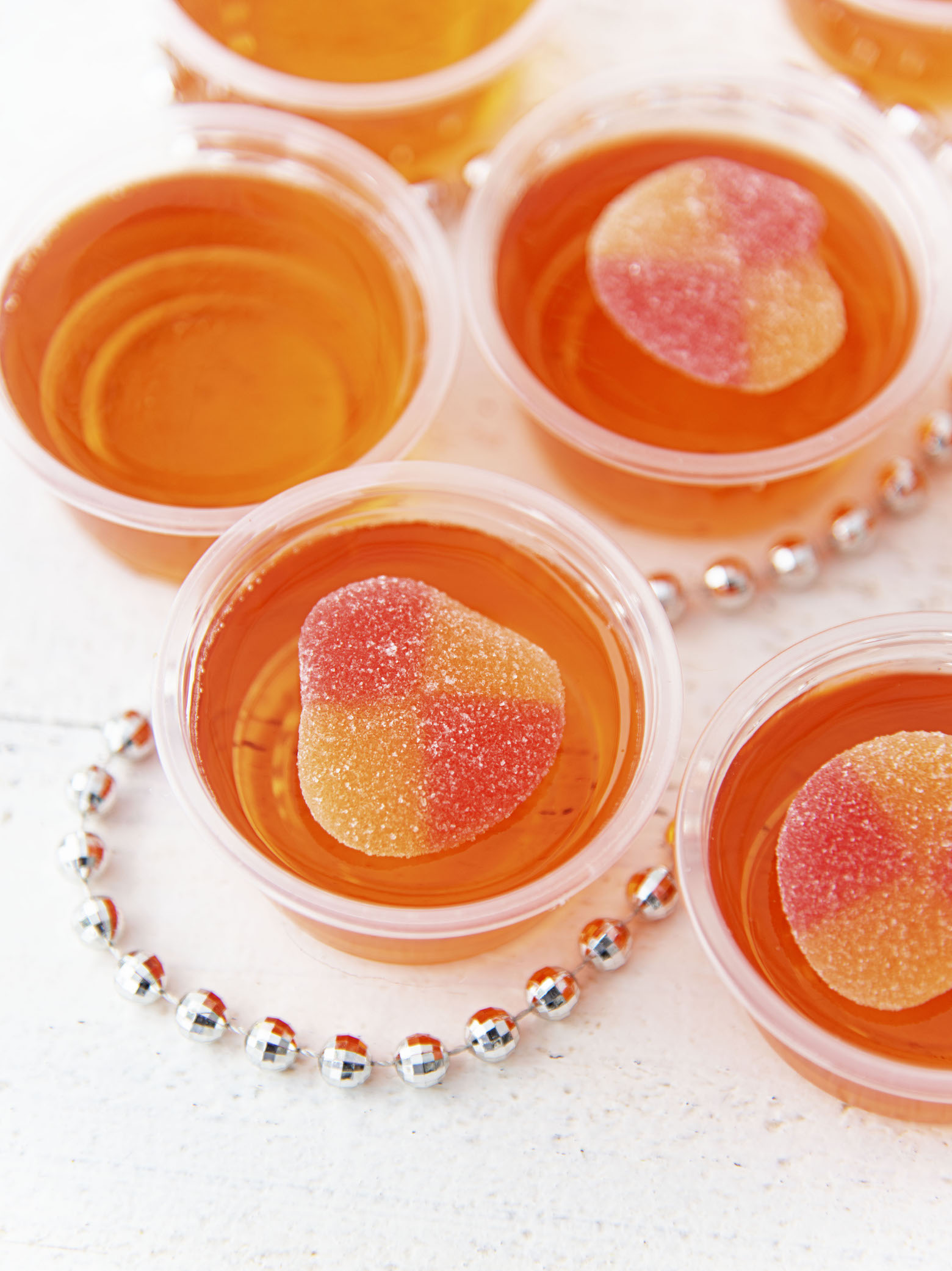 Overhead shots of several peach bellini jello shots with peach gummy candy on top. 