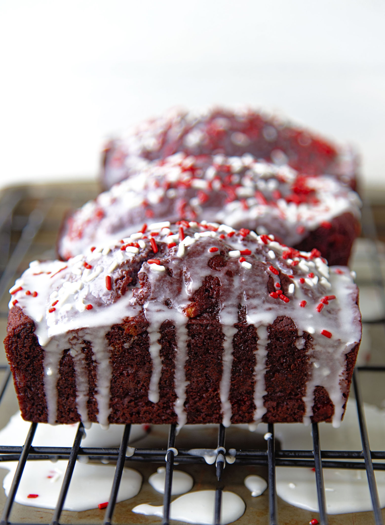 Side view of Peppermint Red Velvet Loaves on a wire rack with icing dripping down. 