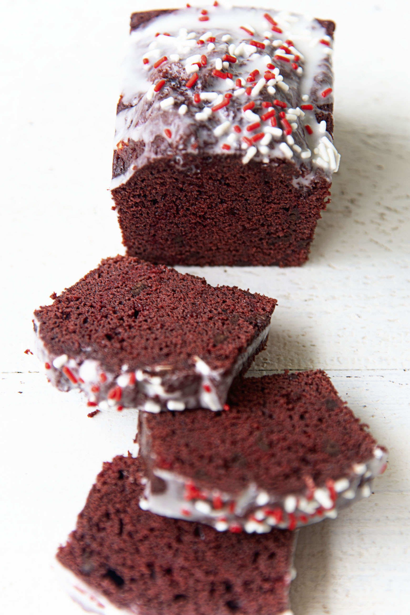 Three quarter shot of the Peppermint Red Velvet Loaf Cake sliced with some pieces laid out. 