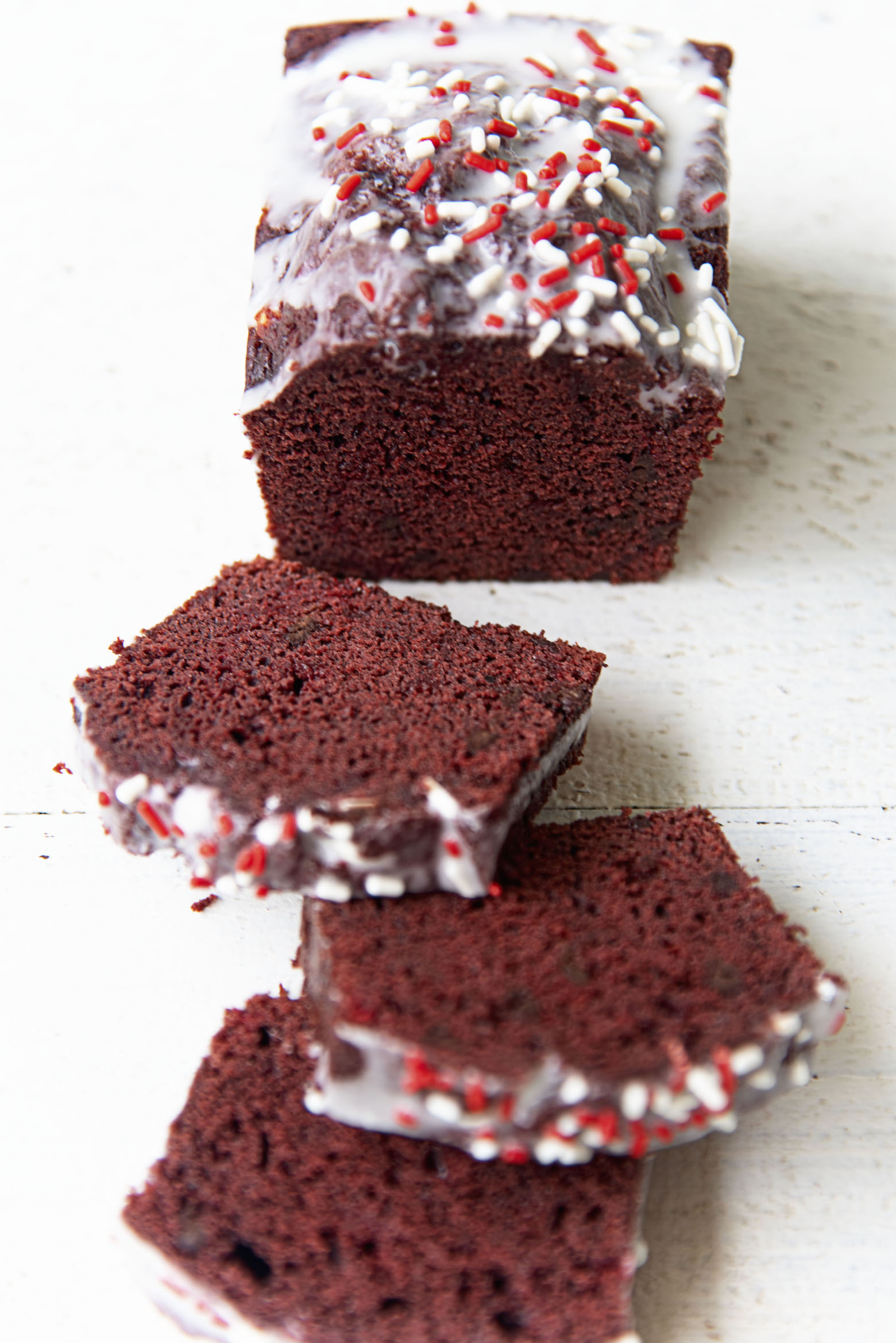 Three quarter shot of the Peppermint Red Velvet Loaf Cake sliced with some pieces laid out.