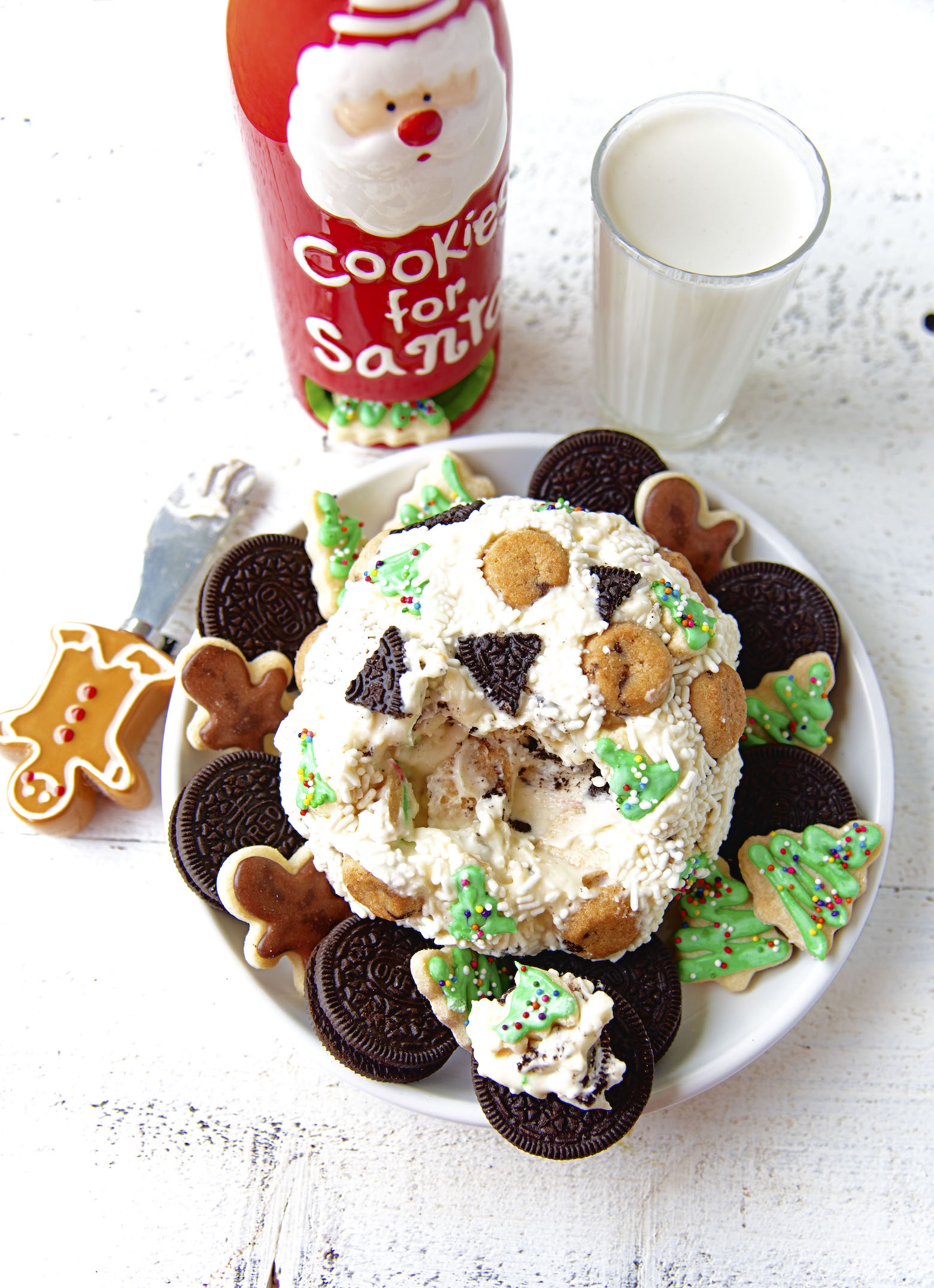 Overhead view of Santa’s Cookies Cheesecake Cheeseball with glass of milk and gingerbread cookie shaped cheese knife. 