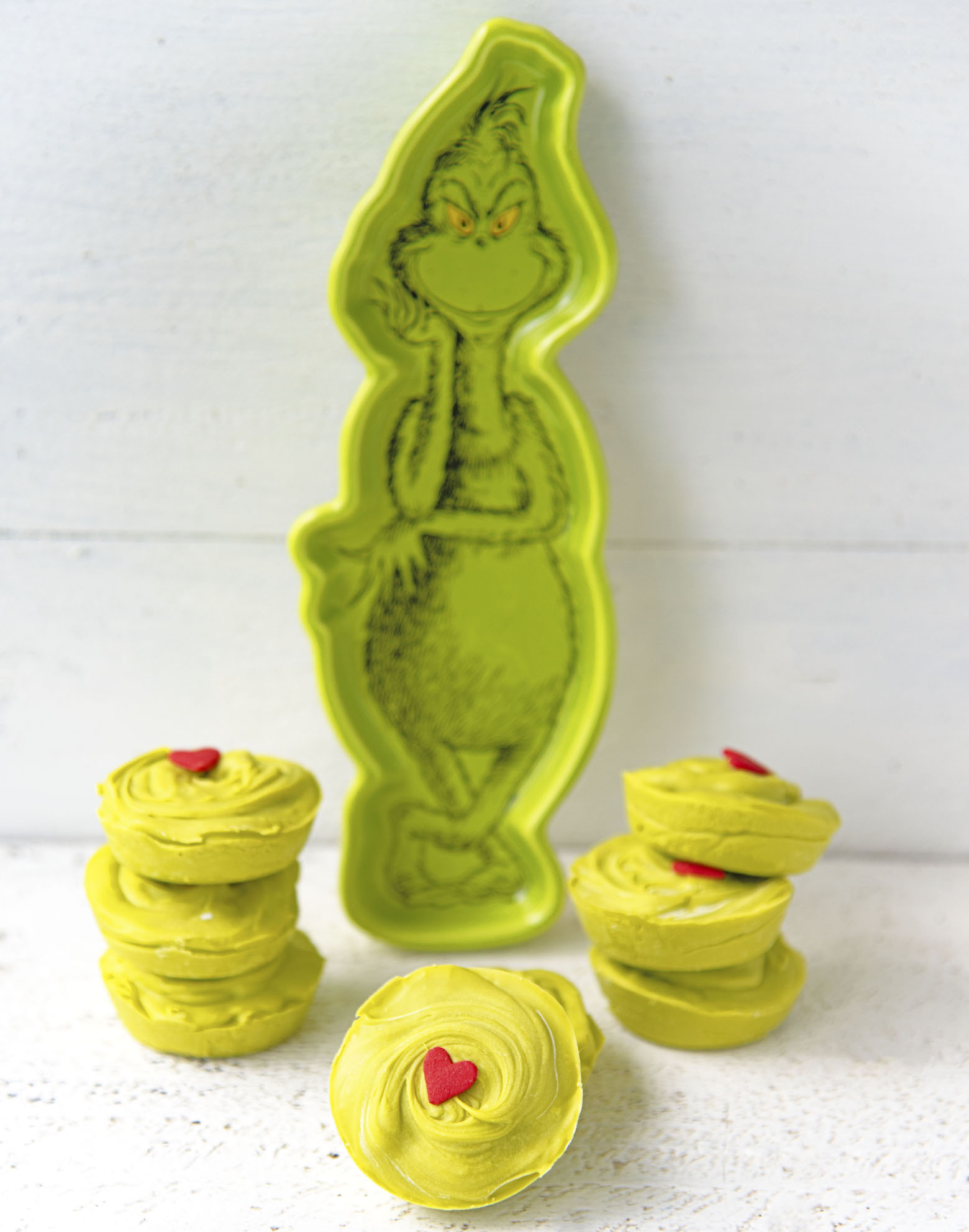 Side shot of The Grinch Sugar Cookie Cups stacked up next to a Grinch dish. 