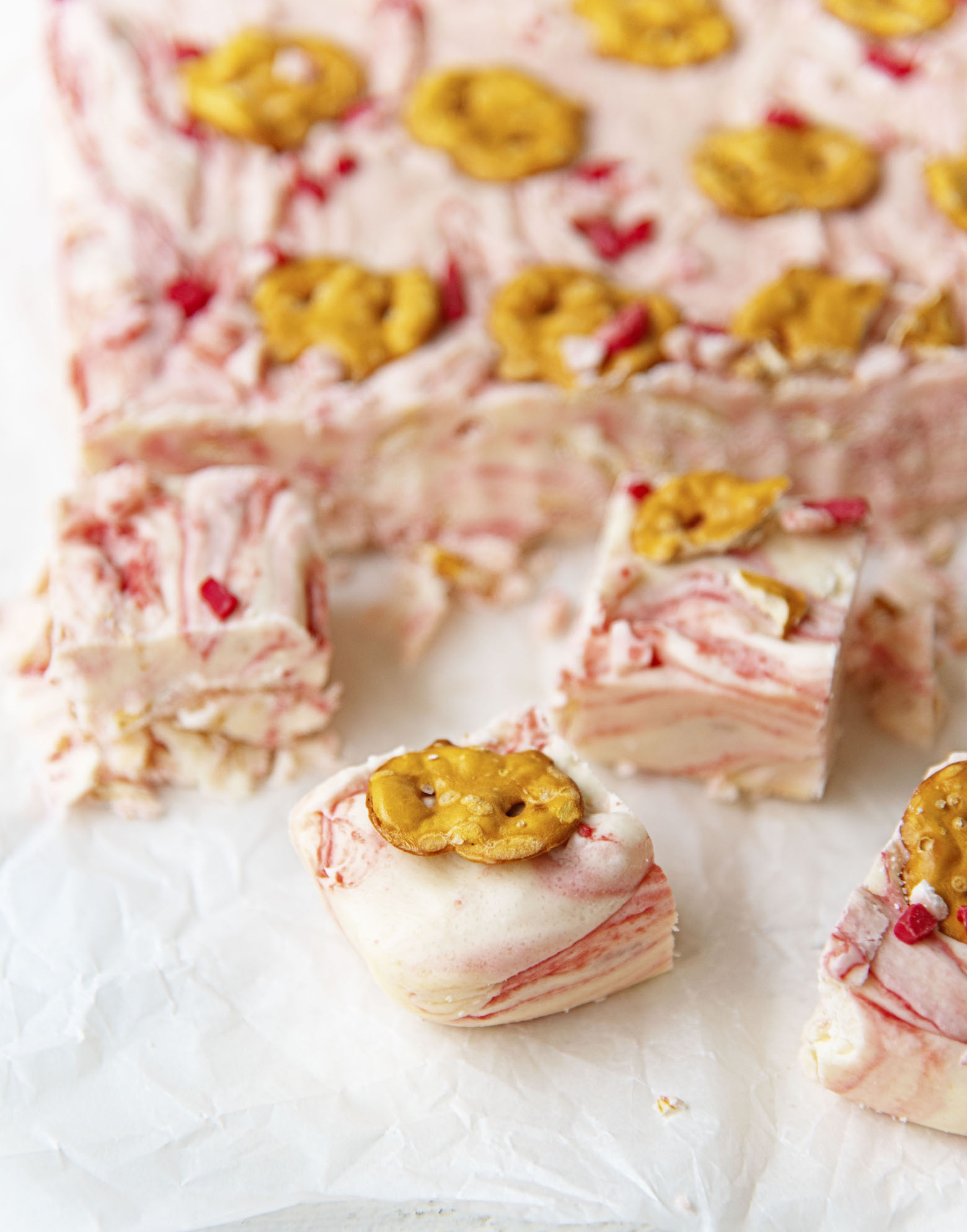White Chocolate Peppermint Pretzel Fudge cut up with a few pieces up front with the remainder of the fudge not cut.