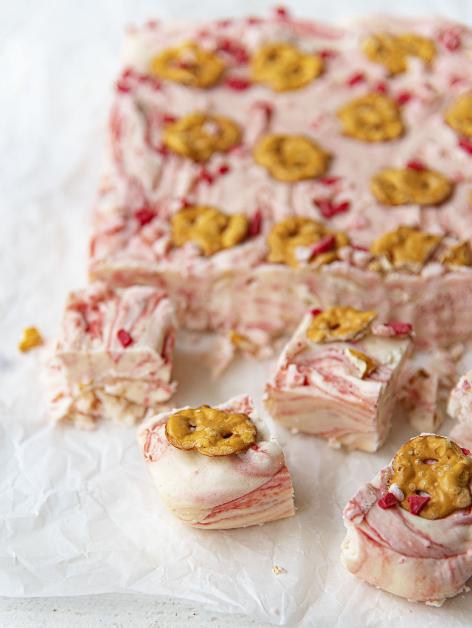 White Chocolate Peppermint Pretzel Fudge with four pieces cut off and scattered. 