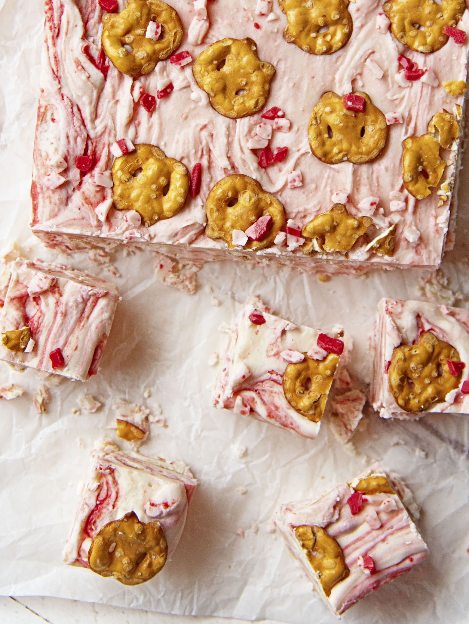 Overhead shot of White Chocolate Peppermint Pretzel Fudge with pieces cut out and scattered. 