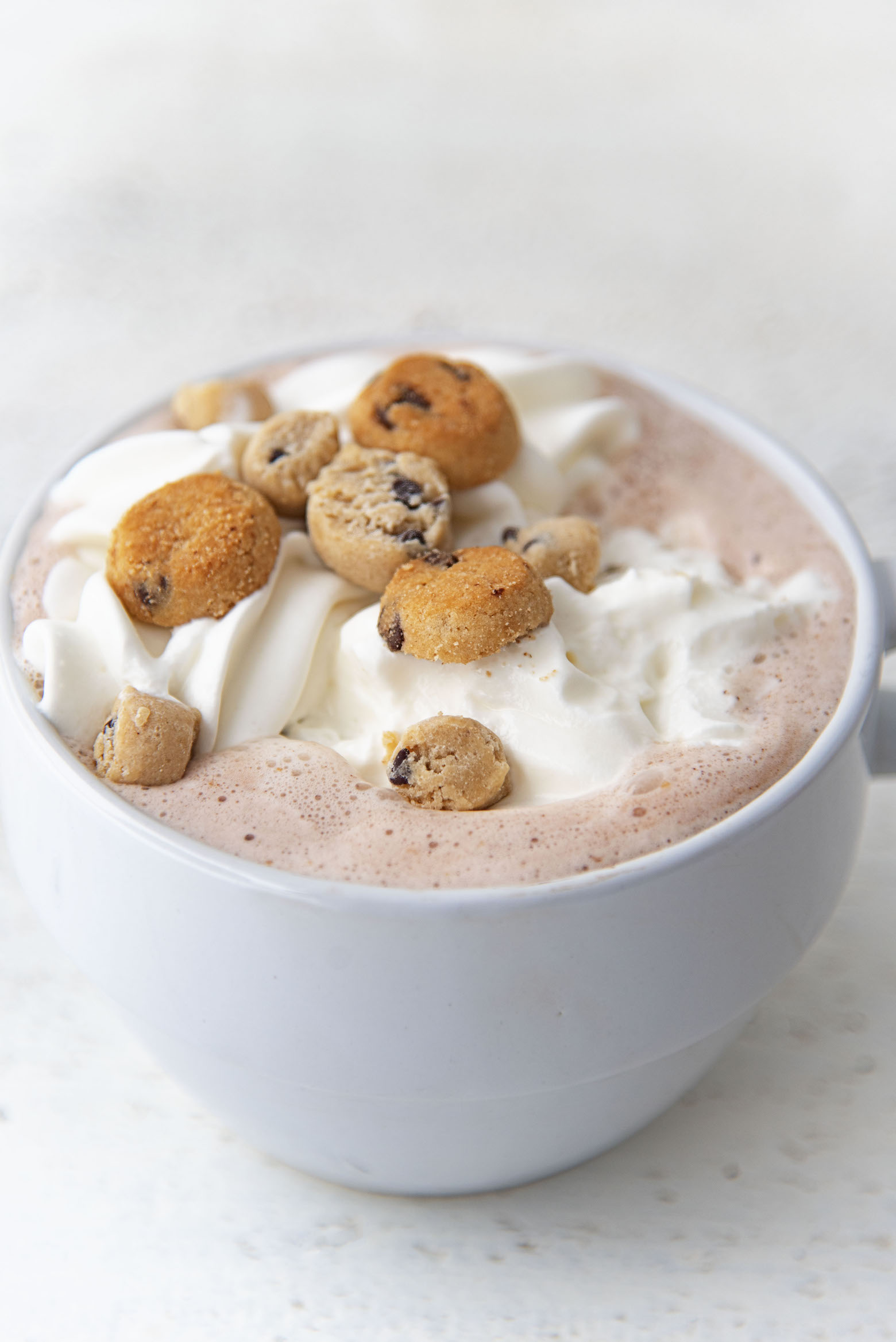 Three quarter shot of  cup of Cookie Dough Hot Cocoa with a focus on the mini cookies on top. 