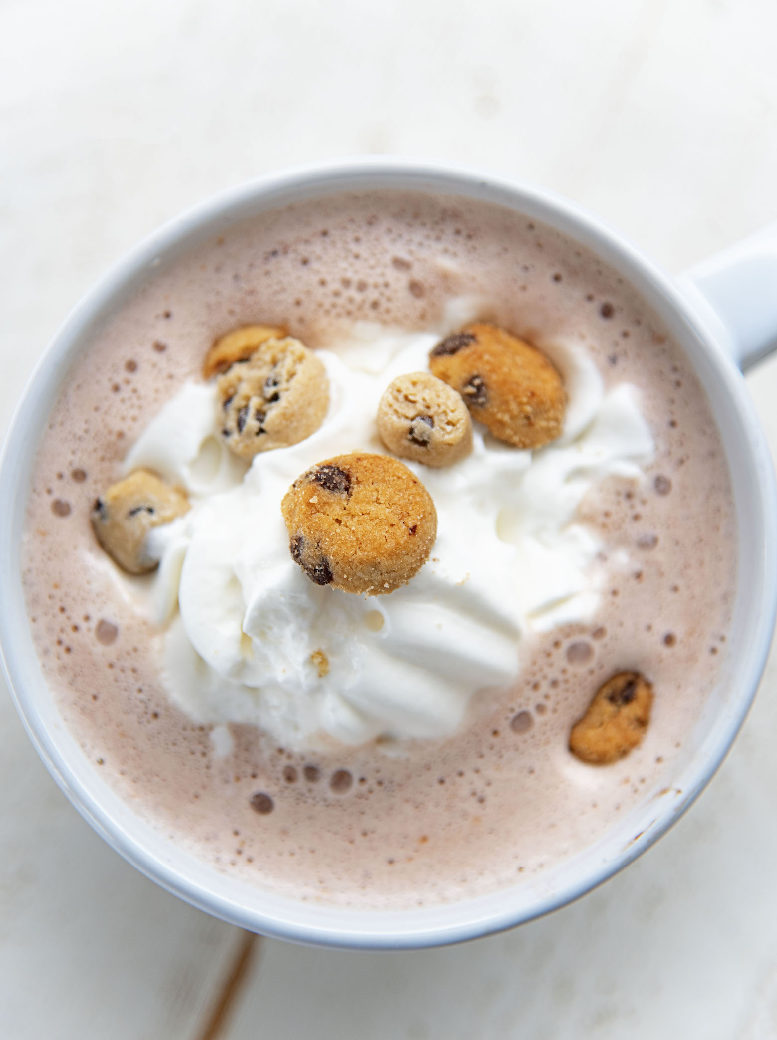 Overhead shot of the cocoa with the main focus on the single mini cookie up top. 