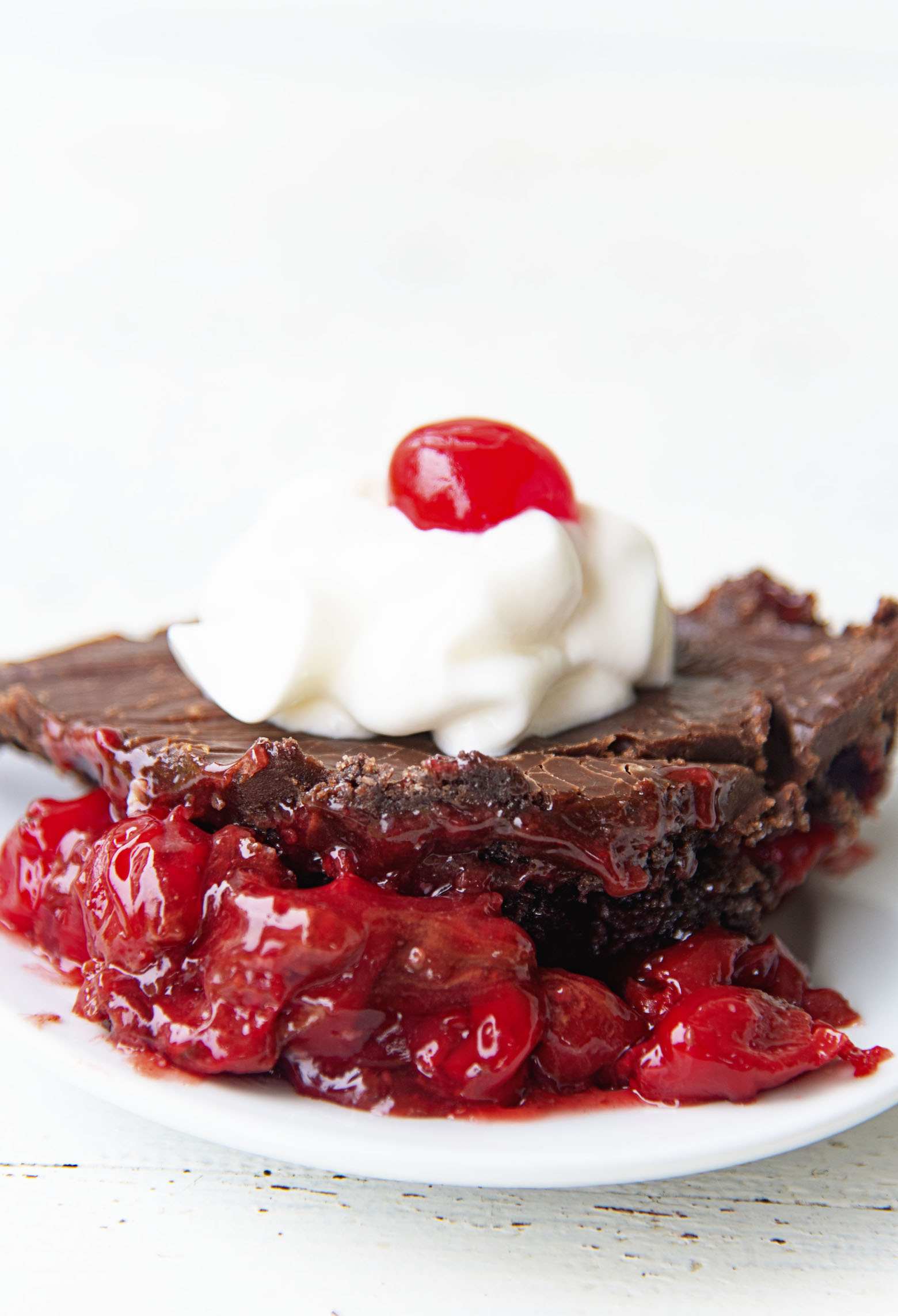 Side view of single scoop of dump cake with whipped cream and cherry on top. 