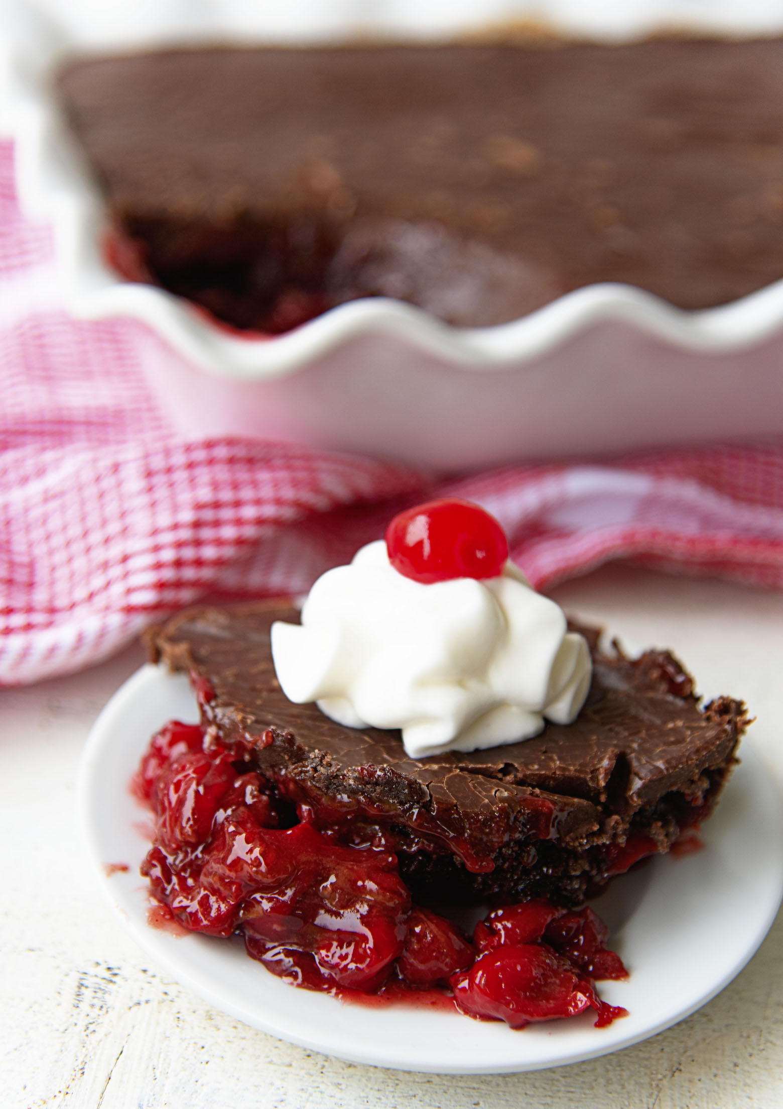 Scoop of Dr. Pepper Chocolate Dump Cake on a plate with remaining cake in background. 