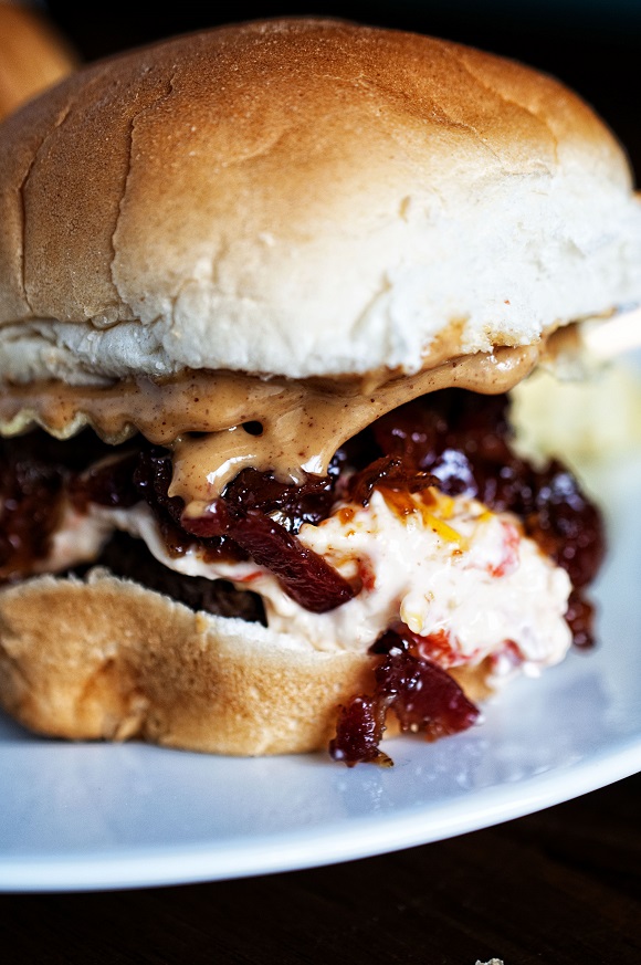 Upclose shot of a slider with the pimento cheese, bacon jam, and peanut butter spilling out. 