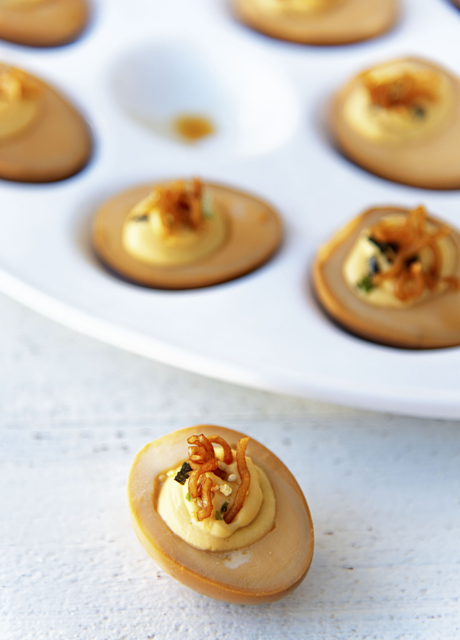 Single deviled egg with egg platter behind it. 