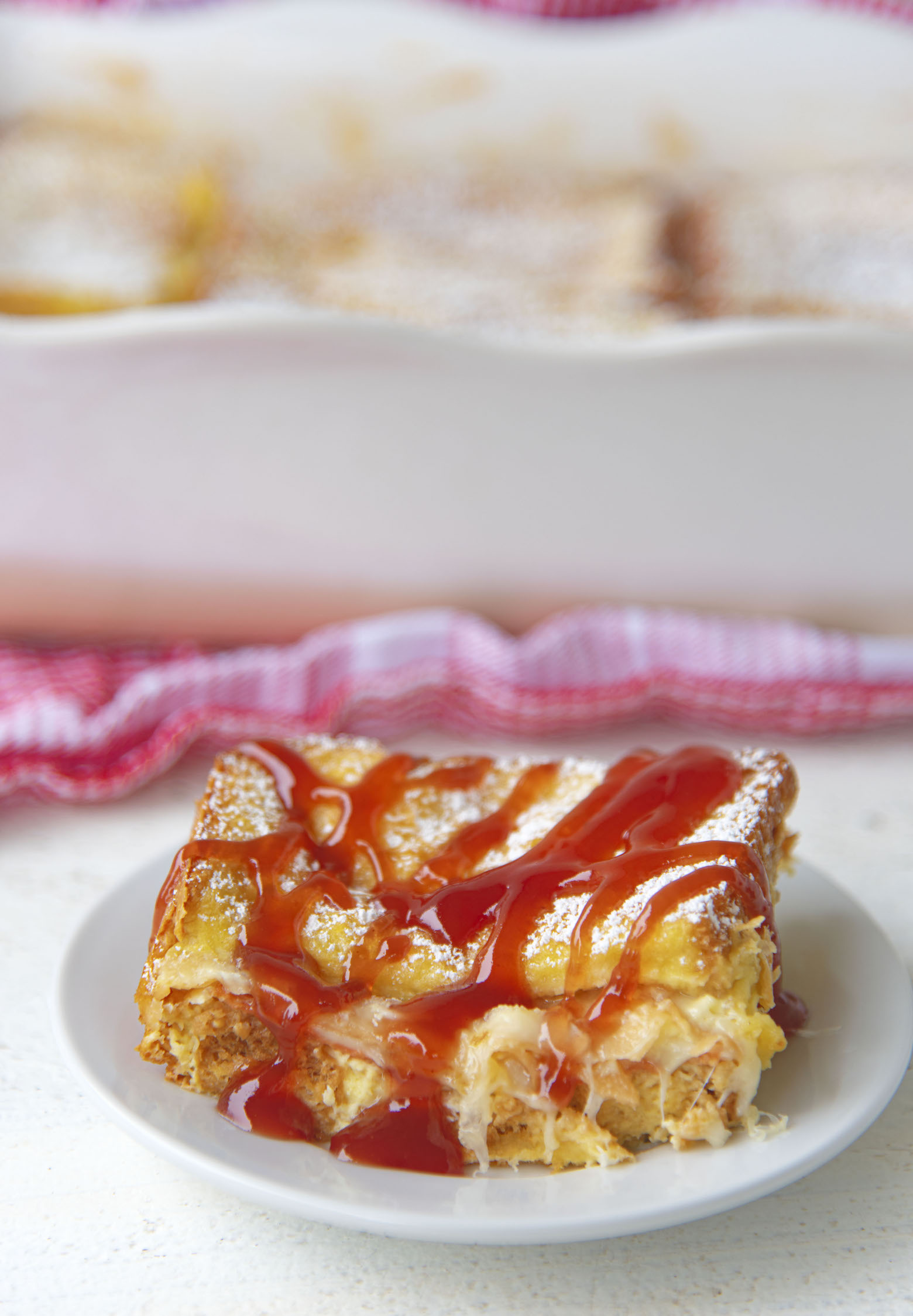 Side view of a slice of casserole with strawberry jam drizzled on it. 