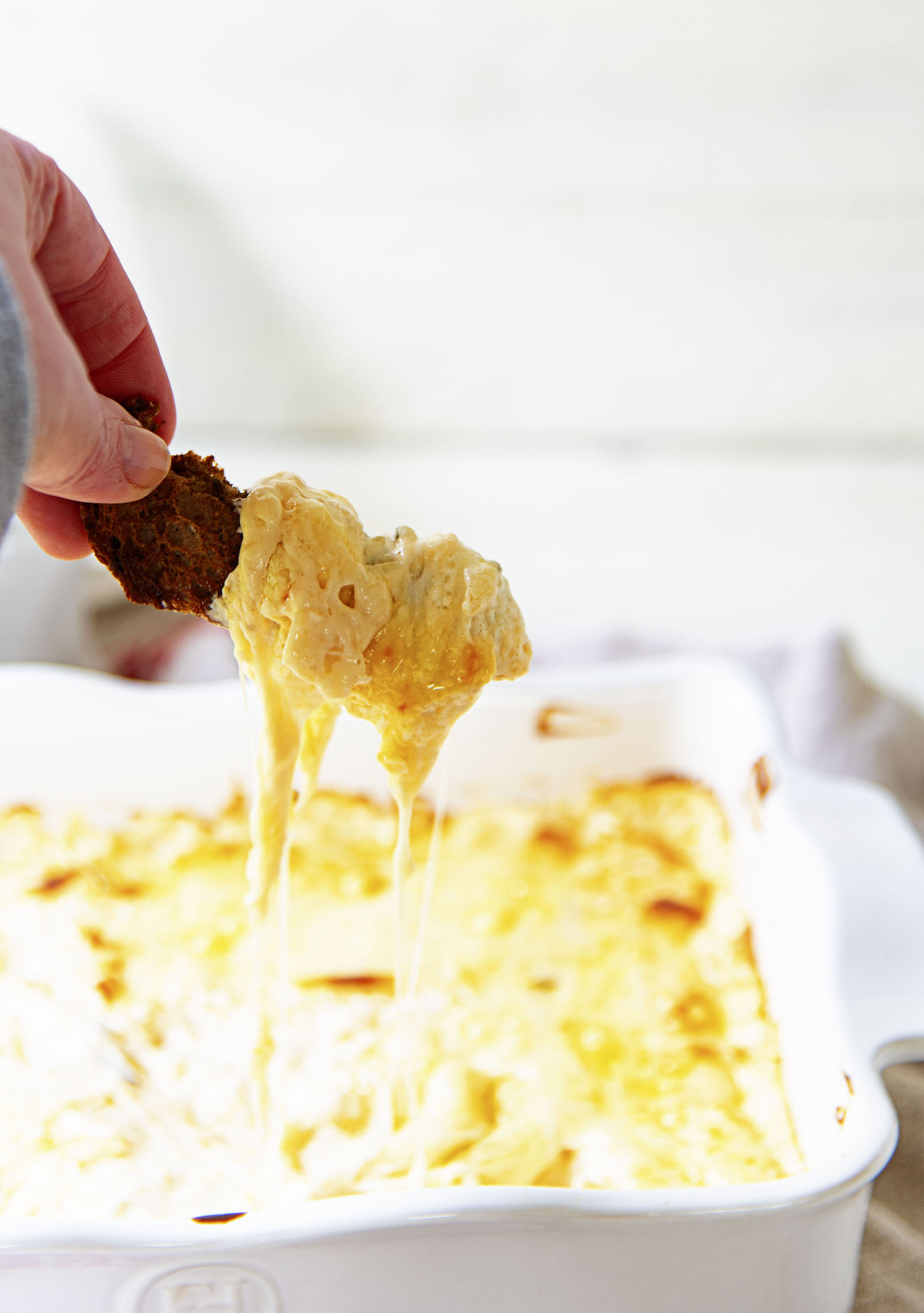 Holding crouton covered in dip with cheese dripping down. 