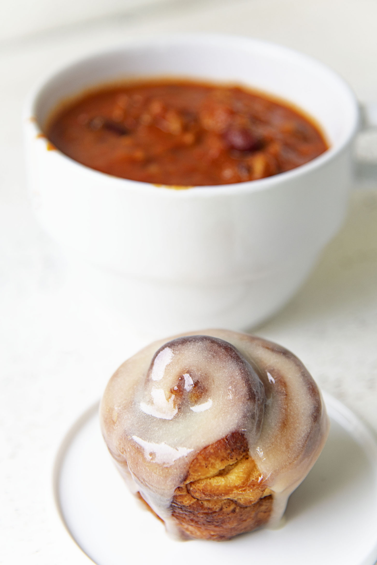 Cinnamon roll on a plate in front of a bowl of chili. 