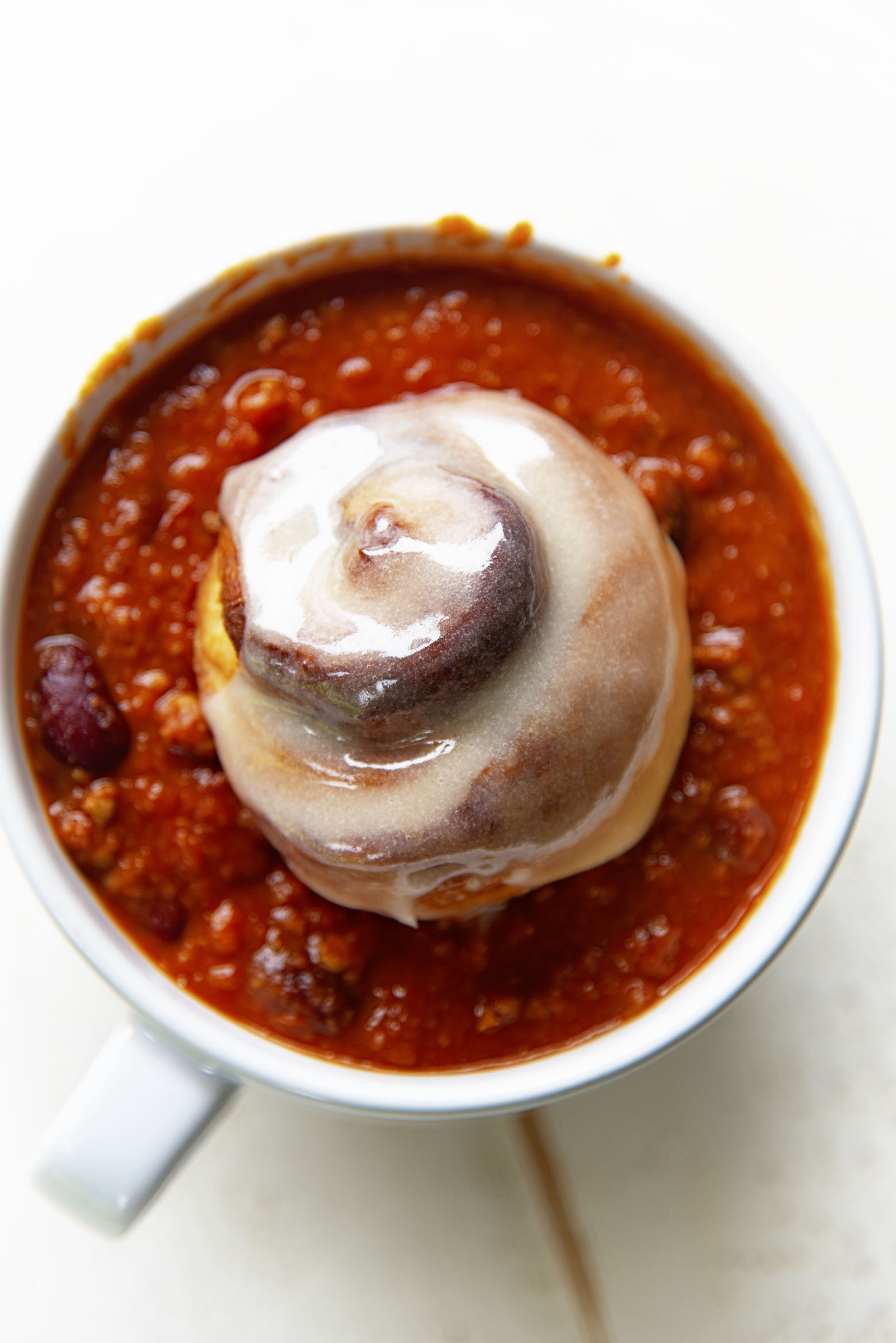Overhead shot of cinnamon roll sitting in a bowl of chili. 