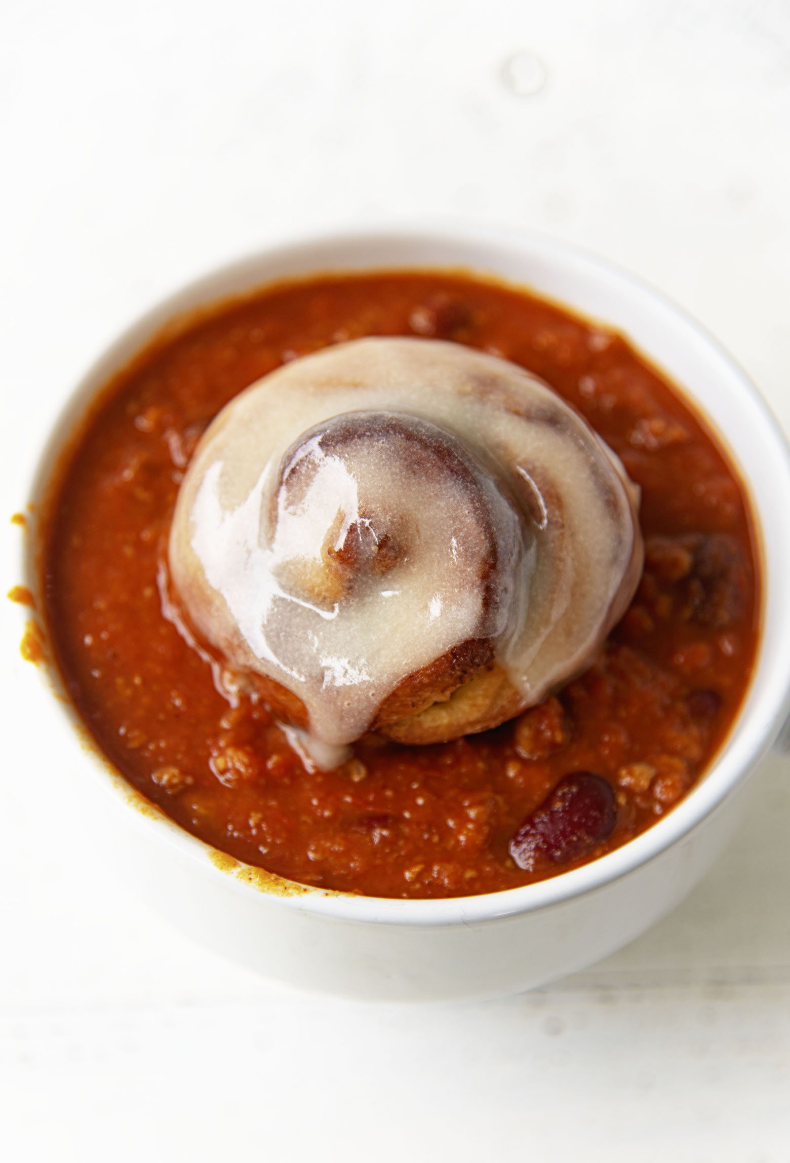 Glazed cinnamon rolls sitting in bowl of chili, close up shot. 