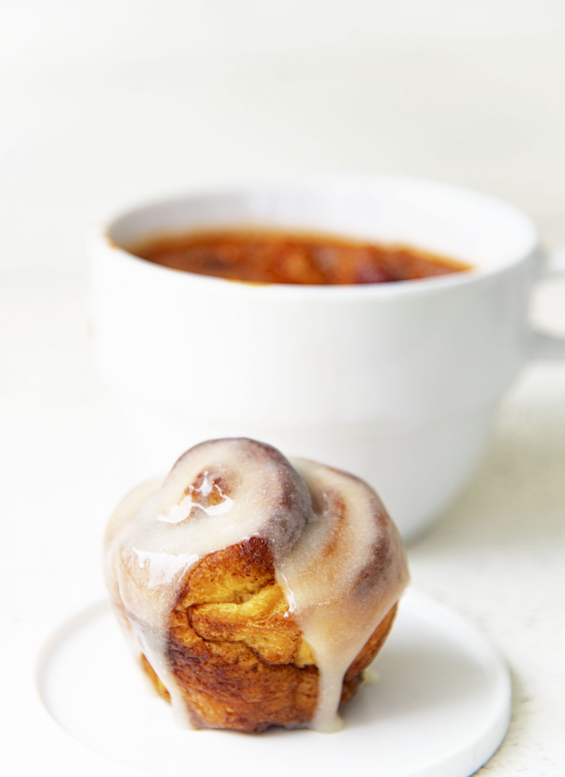 Side view of cinnamon roll with glaze dripping down with bowl of chili in the background. 