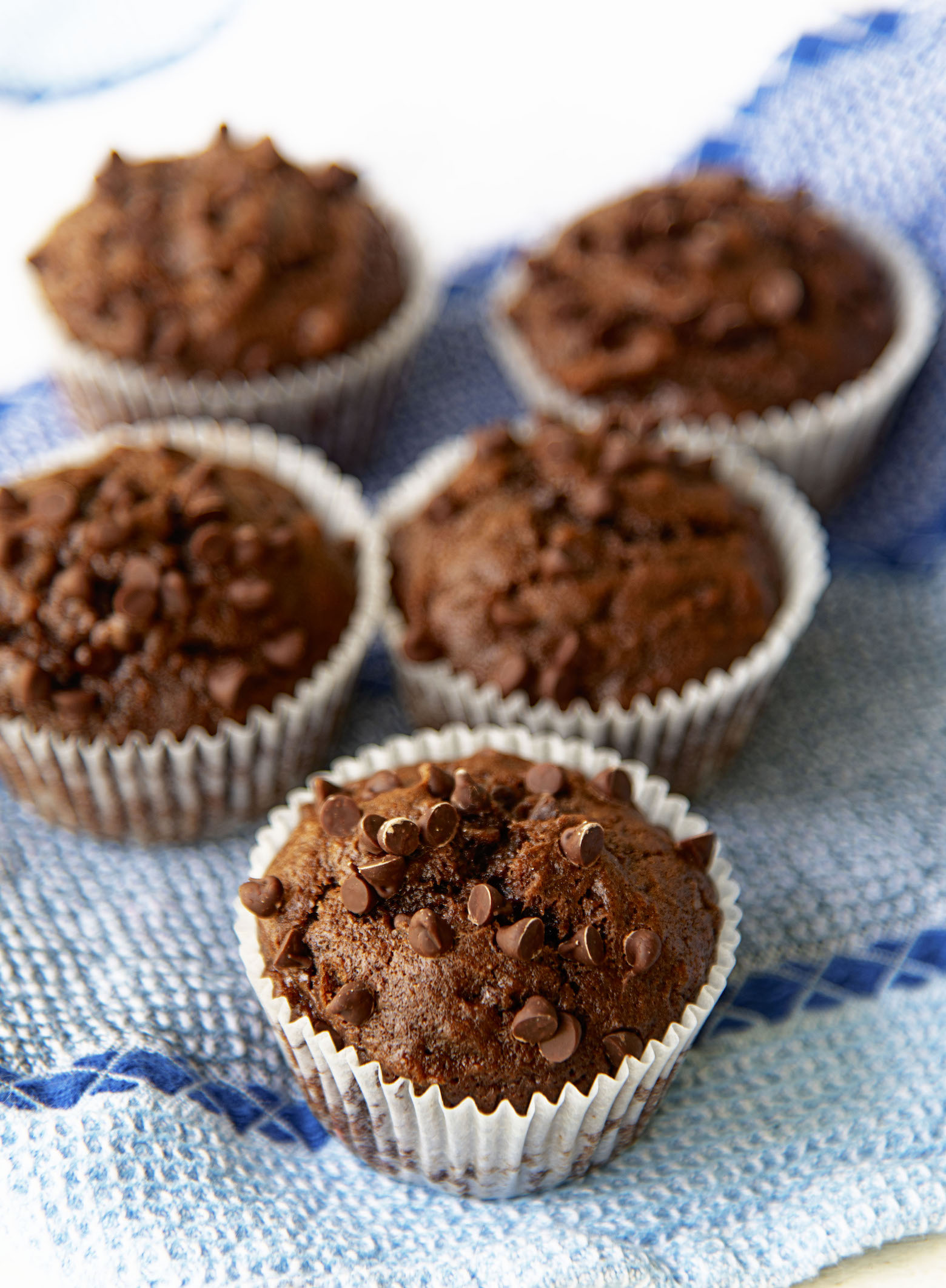 Several Double Chocolate Banana Muffins on a blue kitchen towel. 
