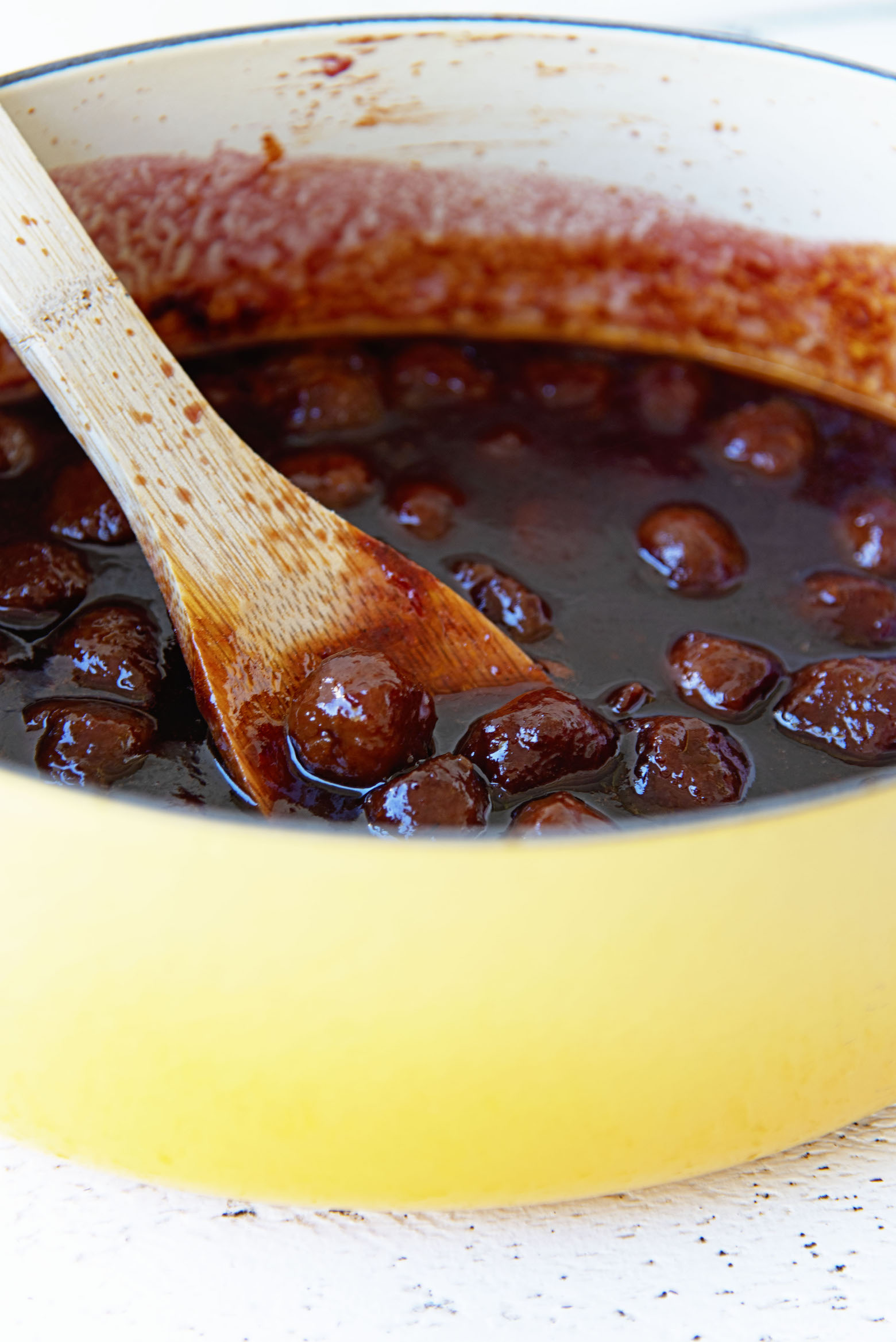 Vegetarian Grape Jelly Meatballs in the pot with a wooden spoon lifting them out of the pot. 