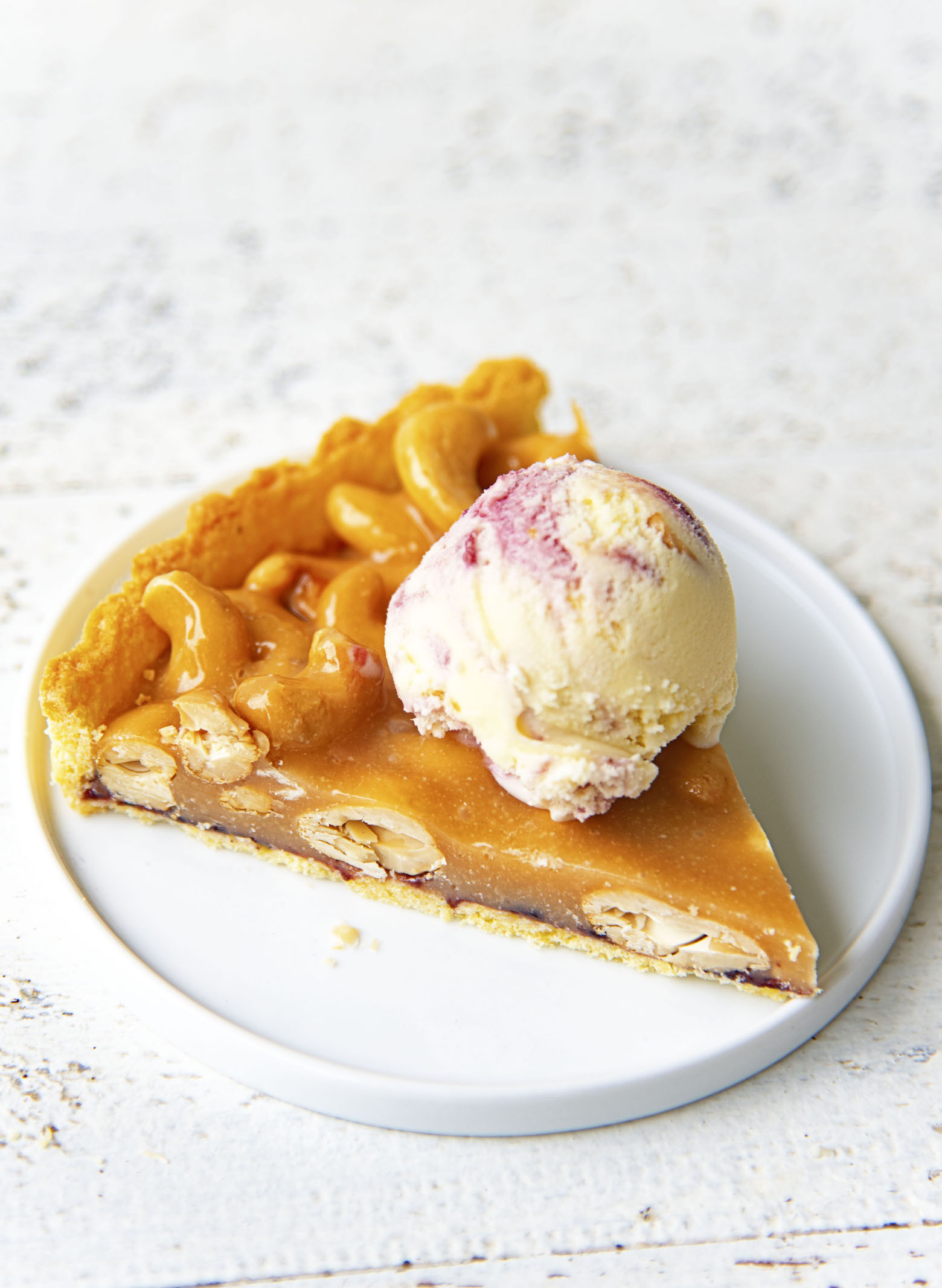 Slice of Baseball Nut Caramel Tart  with ice cream on it on a small white plate. 