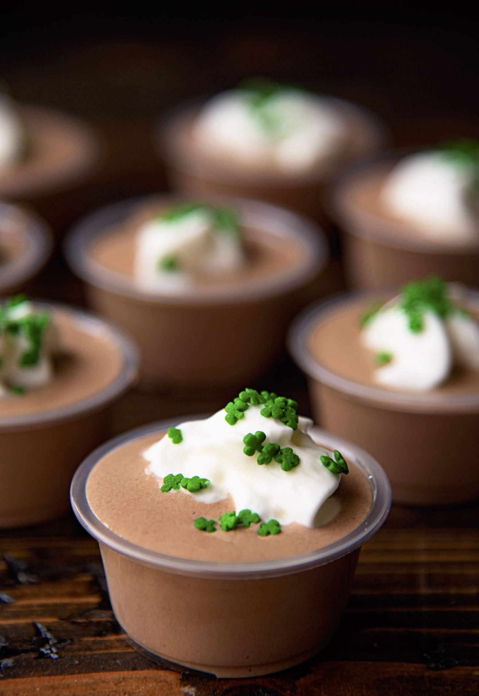 Several Irish Coffee Pudding Shots together with whipped cream and shamrock sprinkles on them. 