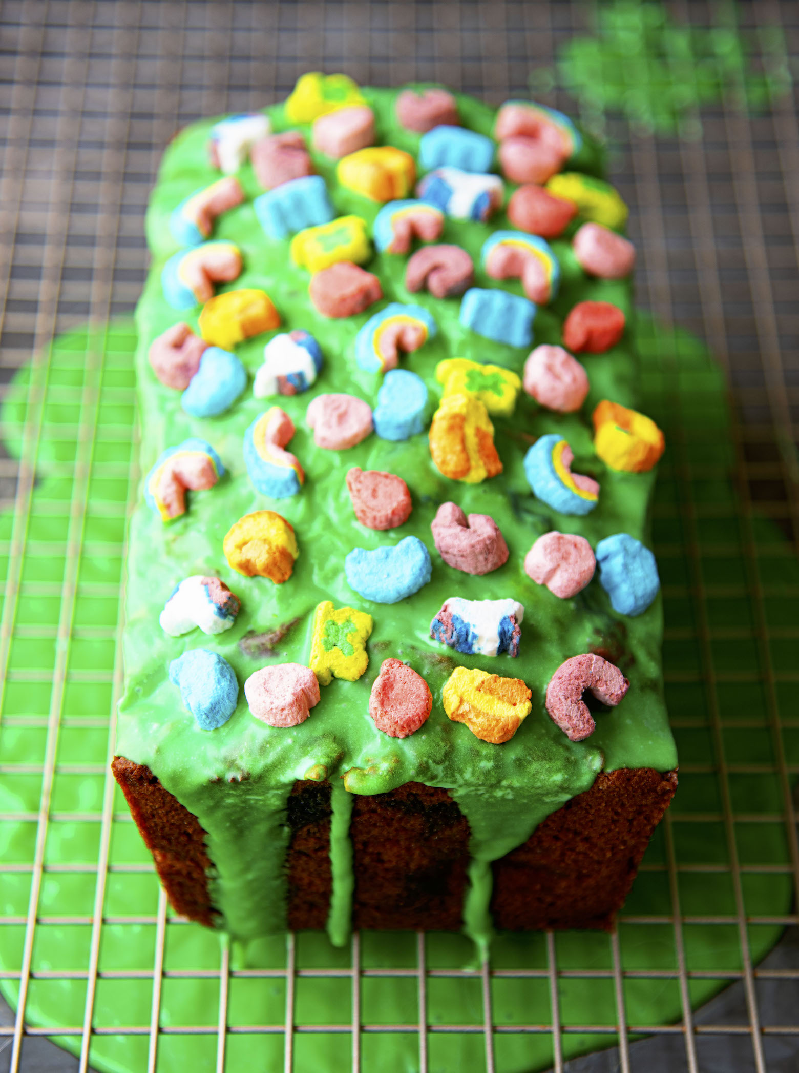 Lucky Charms Banana Bread on a wire rack with the extra green glaze below the bread on a sheet pan. 