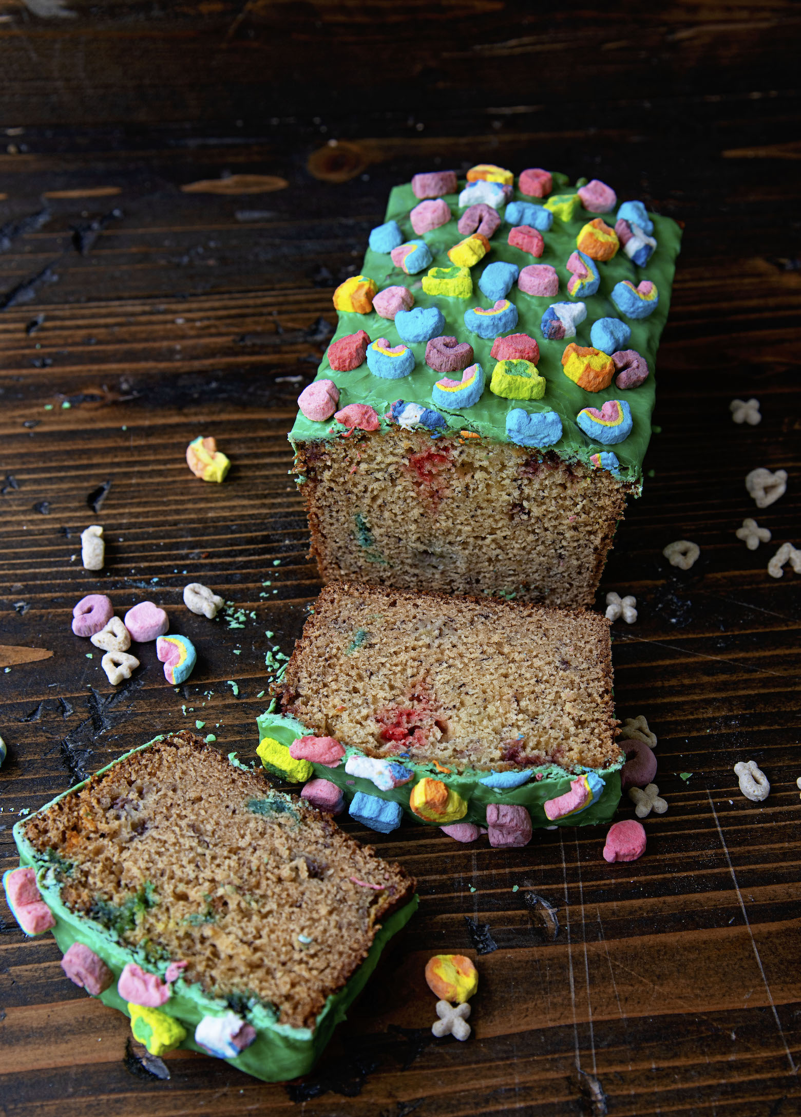 Three quarter shot of Lucky Charms Banana Bread sliced with two slices laying down in front of the loaf. 