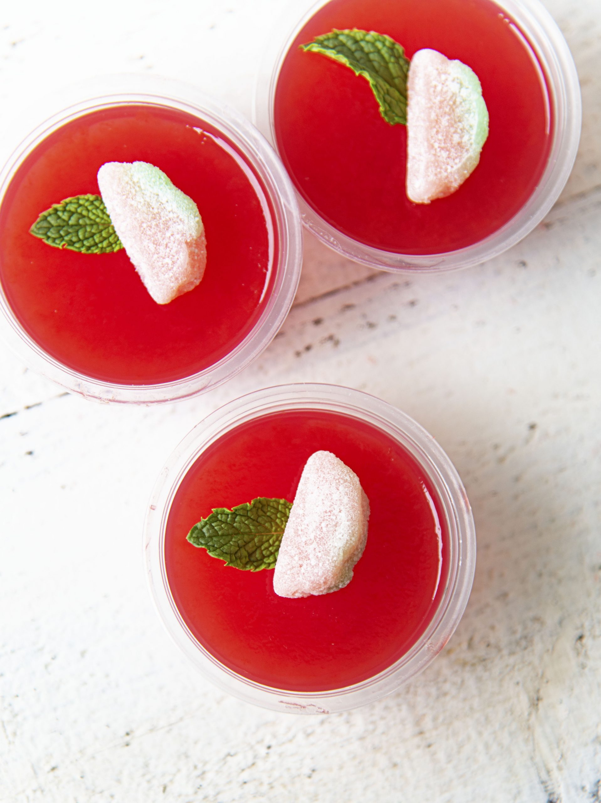 Overhead shot of three Watermelon Mint Julep Jello Shot with mint sprig and watermelon candy on top