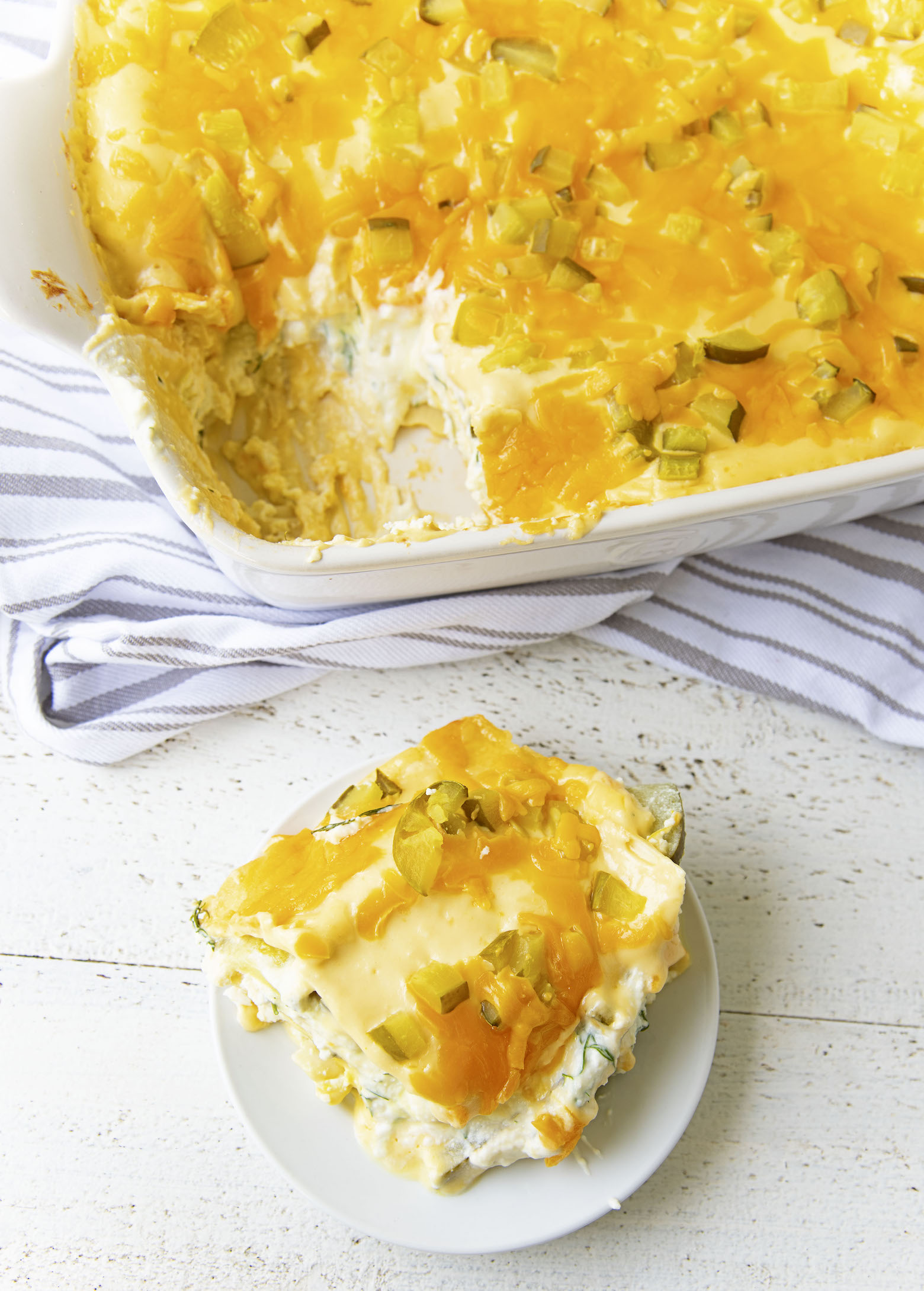 Overhead shot of a piece of Dill Pickle Cheddar Lasagna on plate with remaining lasagna in the casserole dish