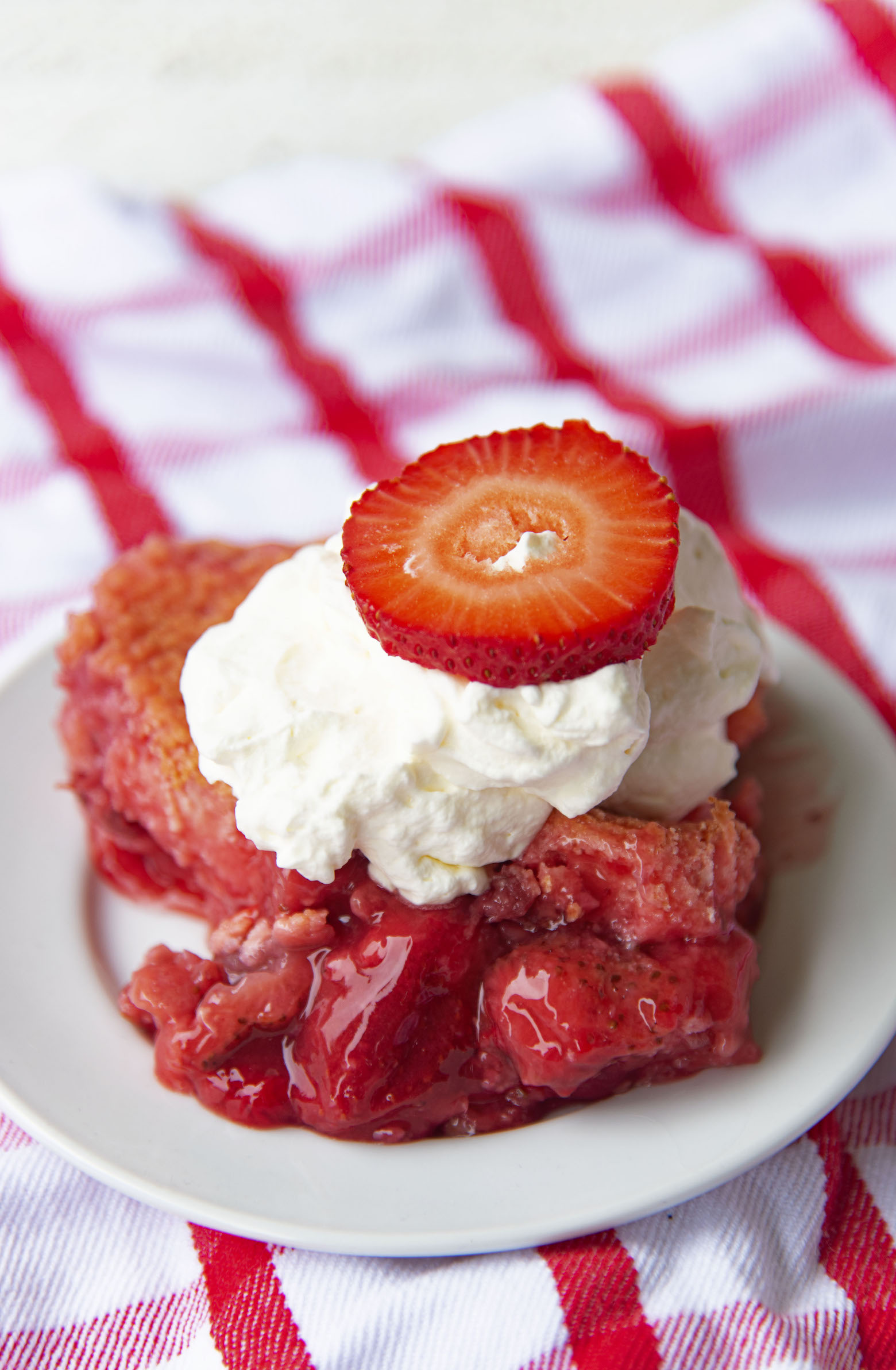 Up close shot of Strawberry Shortcake Dump Cake on a plate with whipped cream and strawberry on top.