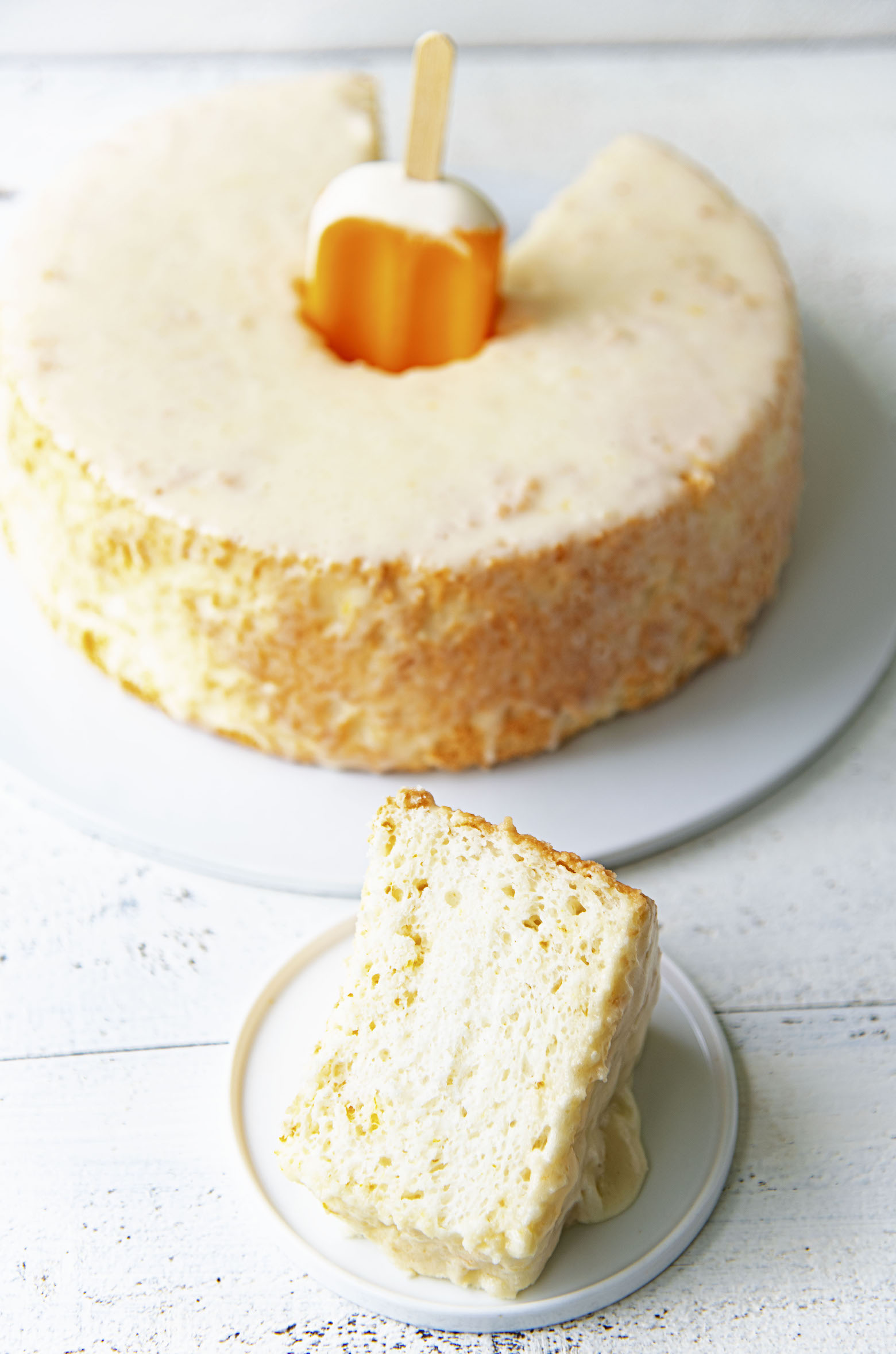 Slice of cake on a plate with remaining cake in background with a creamsicle sticking out of it. 