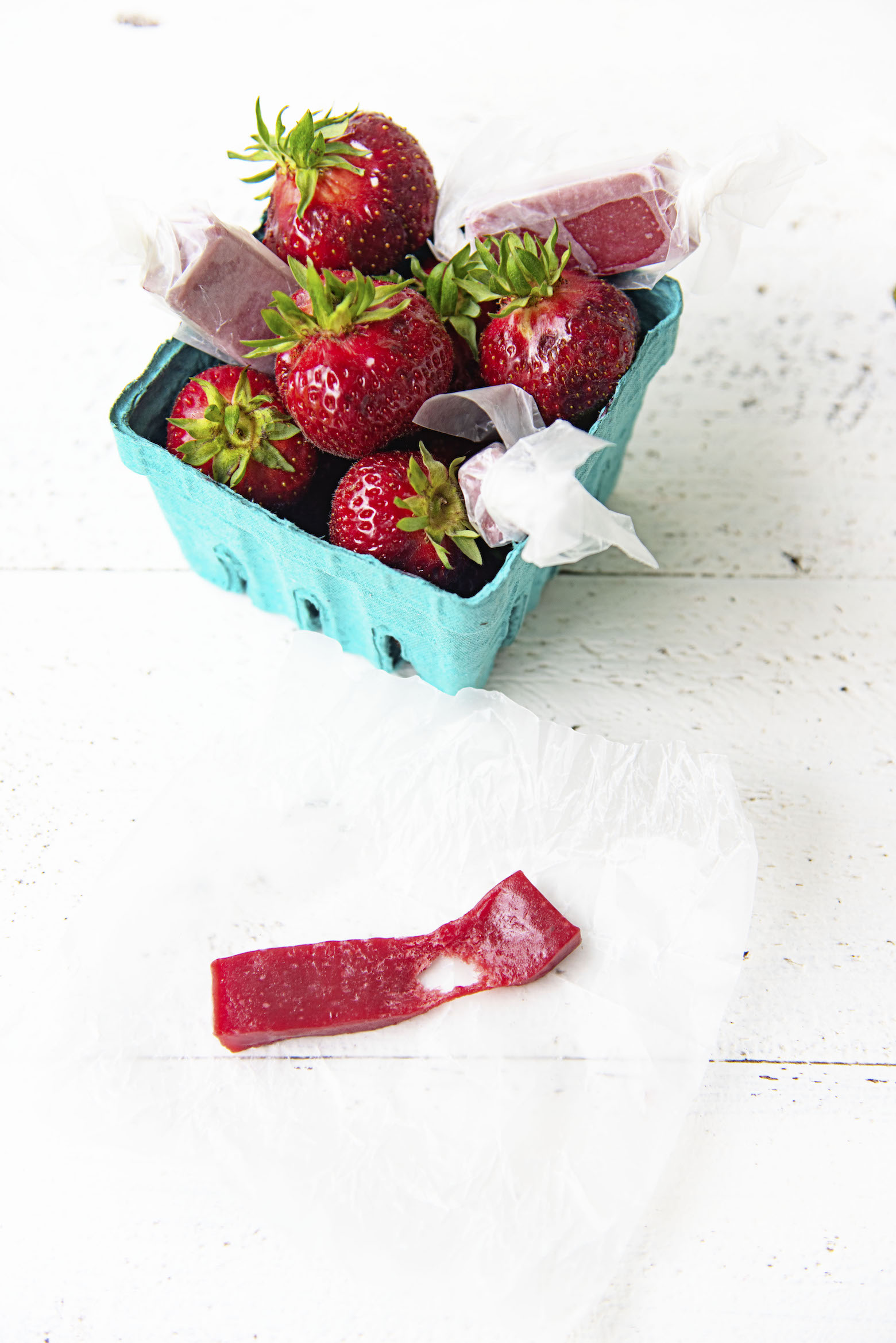 Basket of berries with a caramel stretched out on a piece of wax paper. 