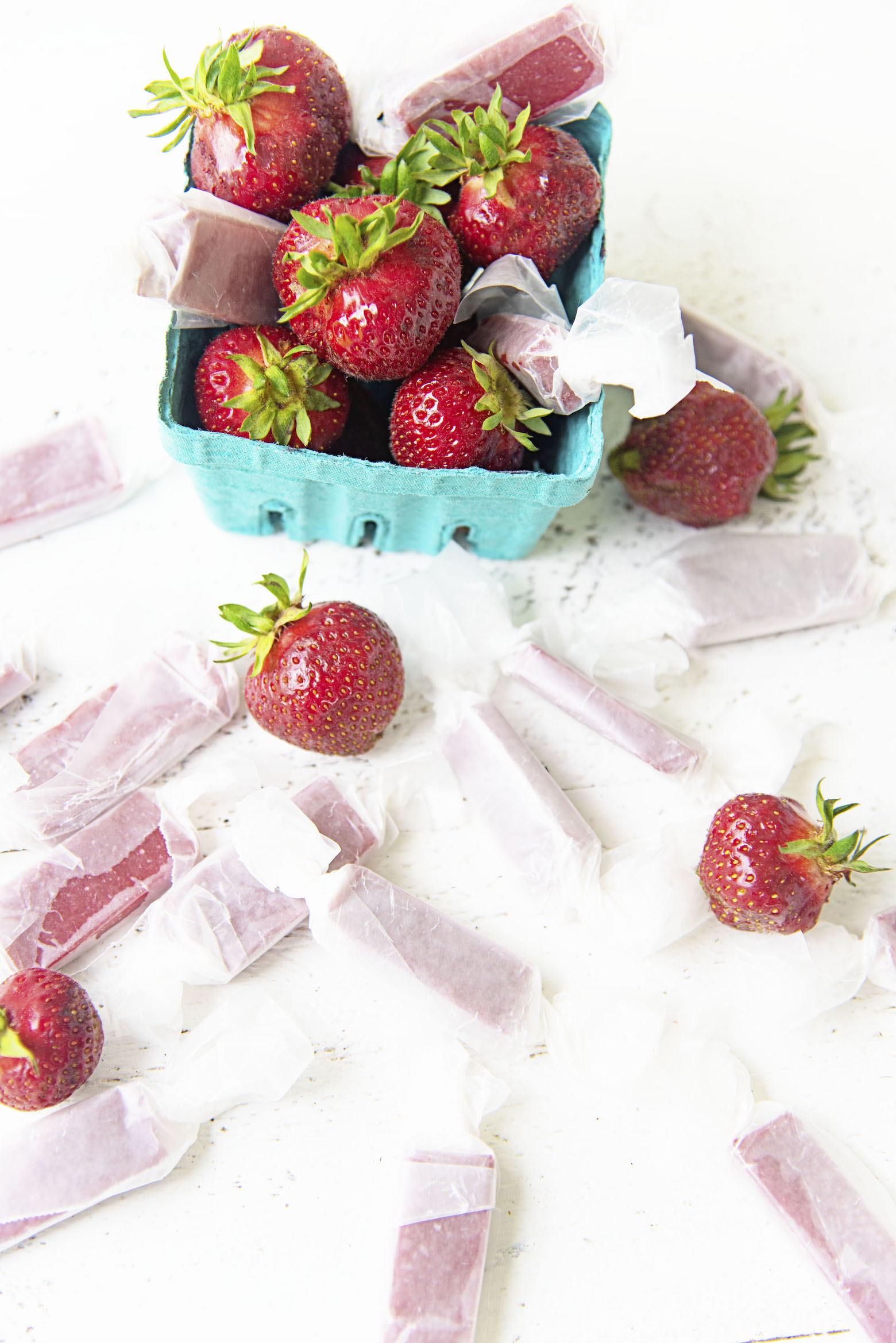 Overhead view of basket of strawberries and scattered Fresh Strawberry Soft Caramels