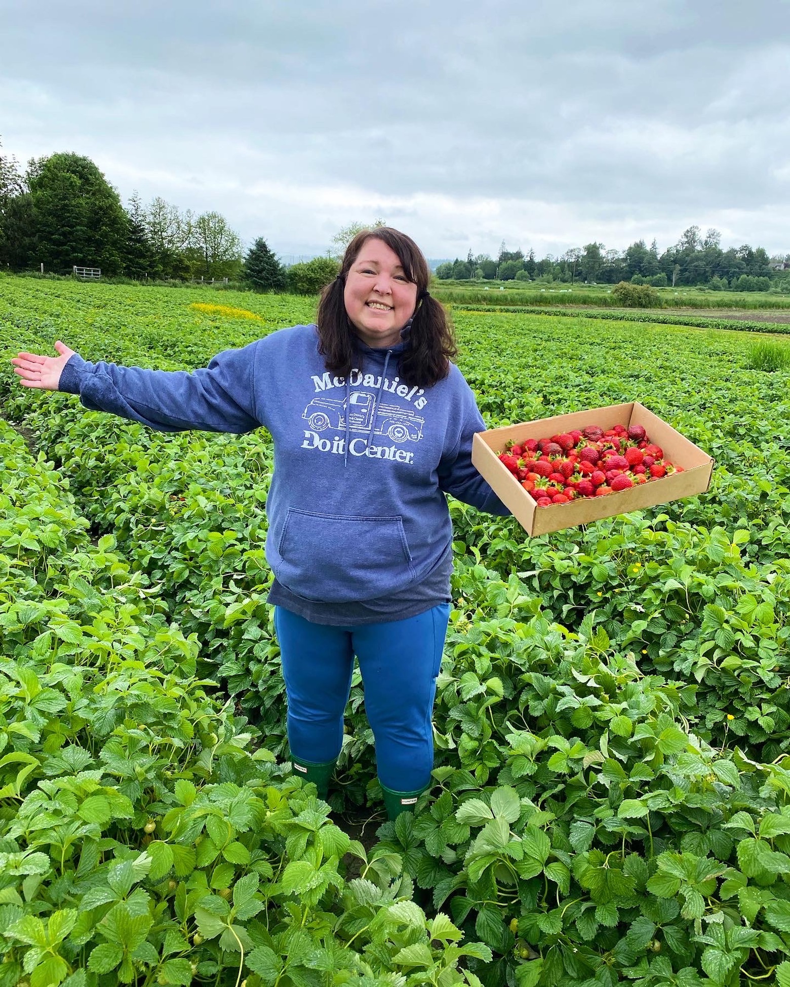 Peabody standing in a field of strawberries holding a box of strawberries. 