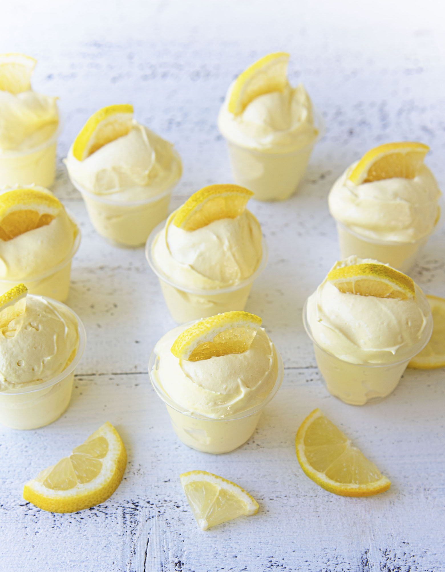 Gathering of Frosted Lemonade Pudding Shots with lemon slices around them. 