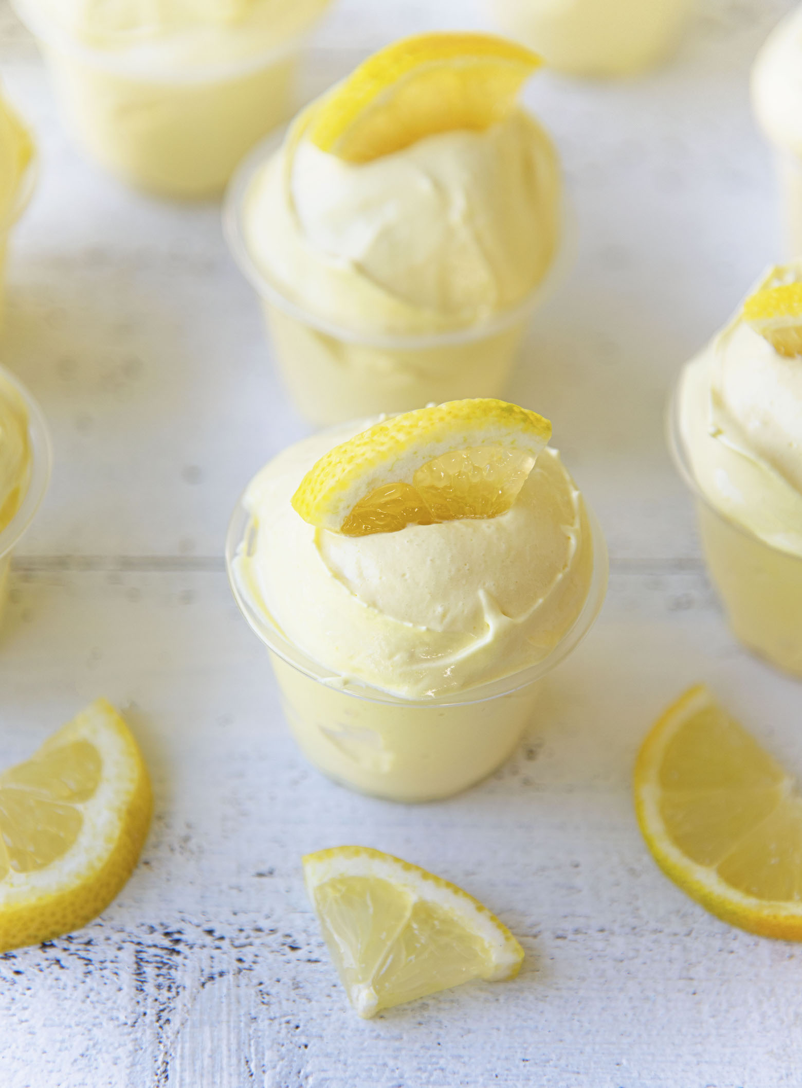 Three quarter shot of Frosted Lemonade Pudding Shots with lemon slices around them.