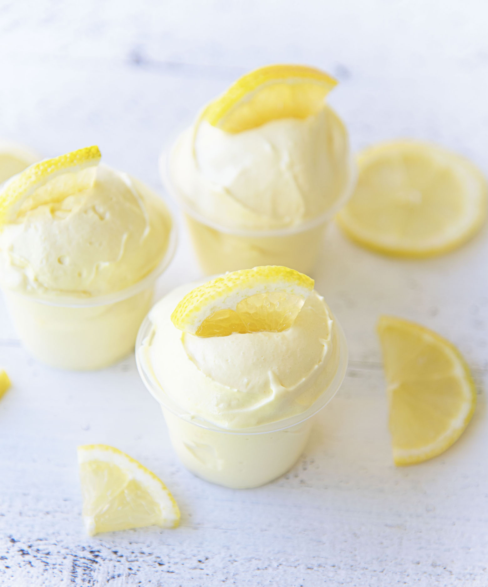 Overhead of three Frosted Lemonade Pudding Shots with lemon slices around them. 