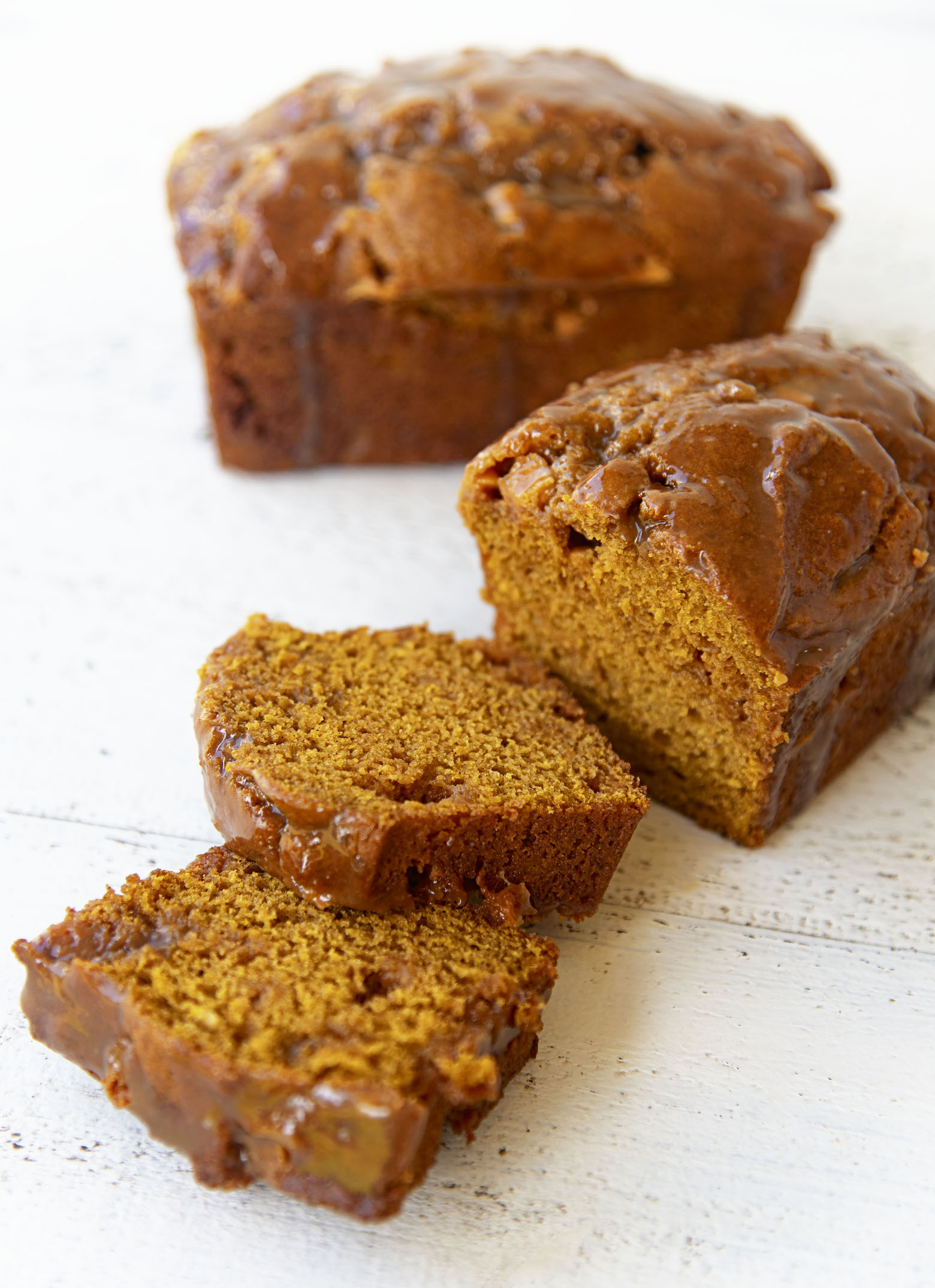 One whole pumpkin bread in the background and one bread up front with two slices cut out of it.