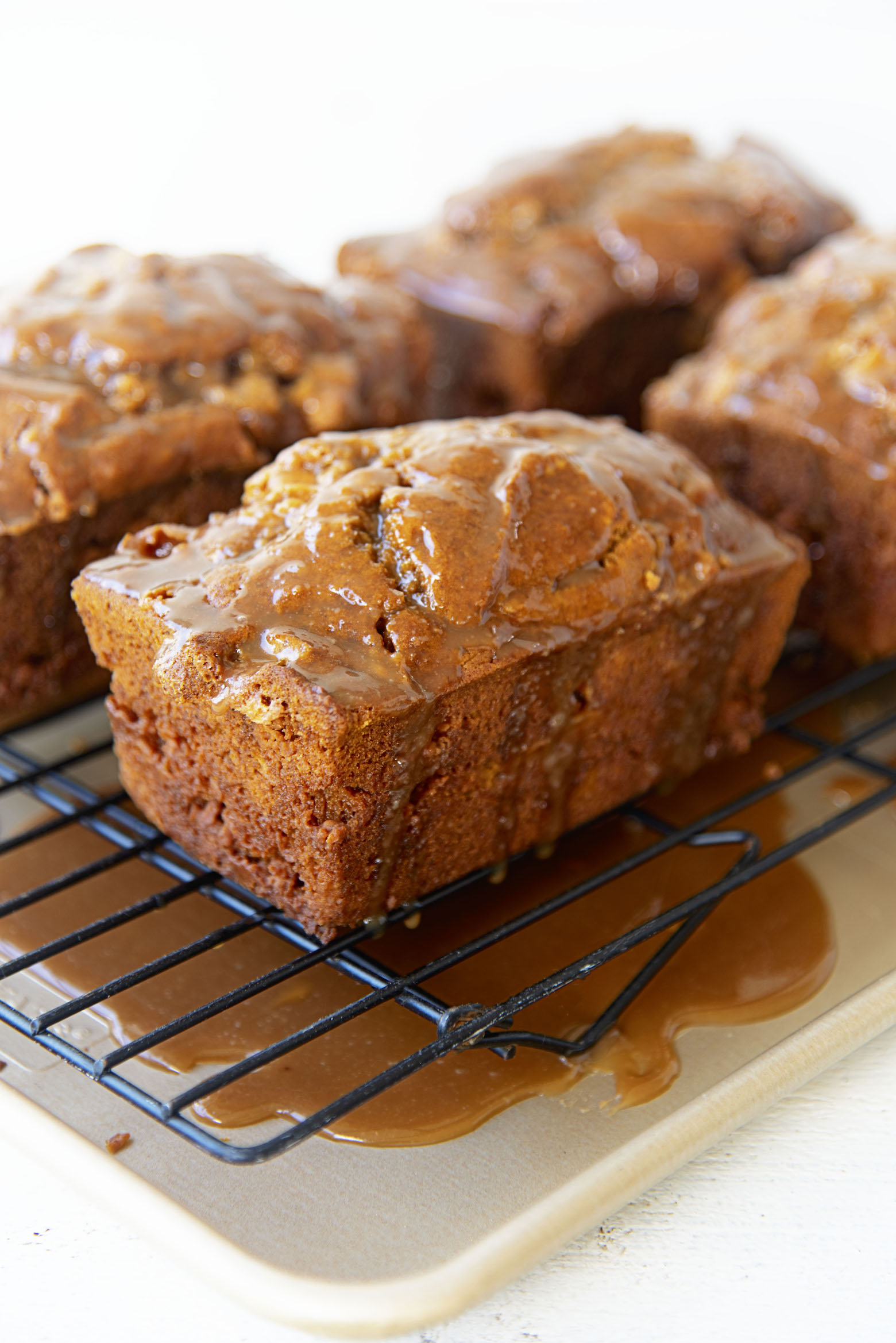 Several pumpkin breads on a wire rack with glaze on them with the glaze underneath the wire rack on a baking sheet.
