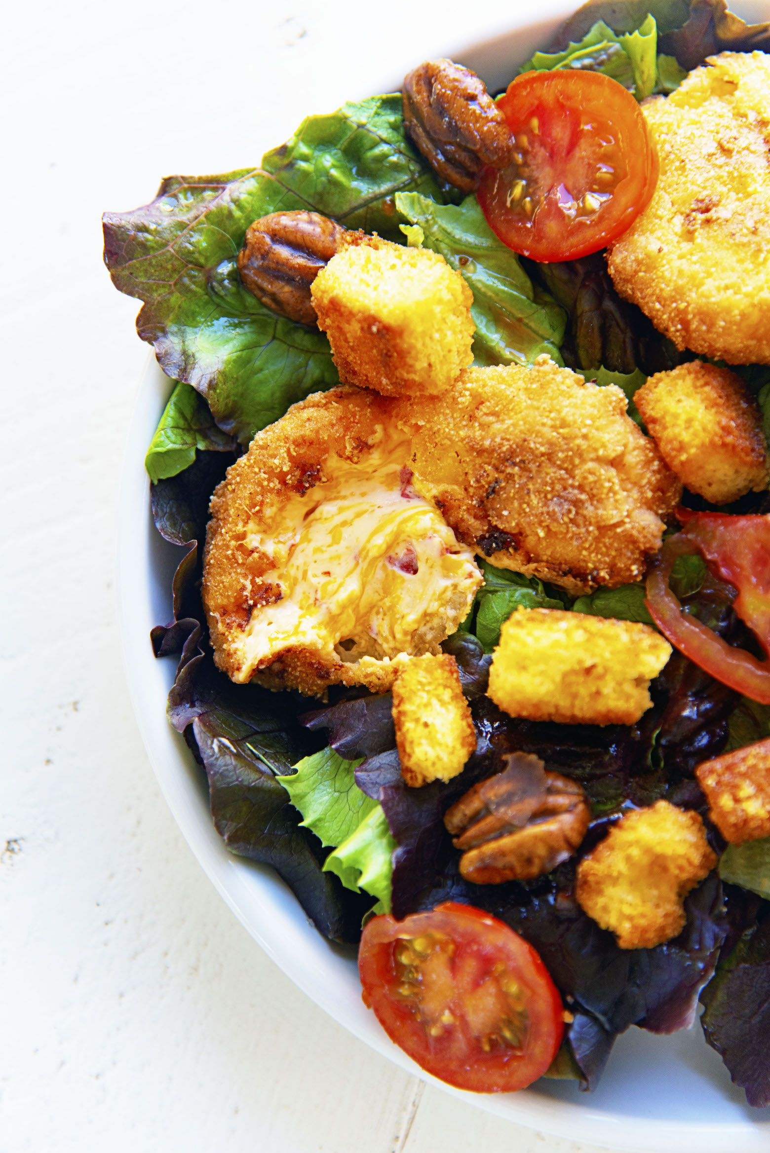 Close up of fried pimento cheese pulled apart on top of salad.