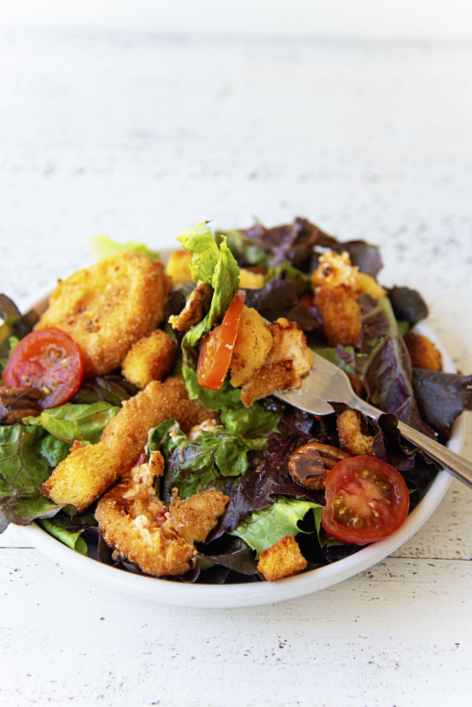 Close up of fork full of salad with the remaining salad down below on a plate. 