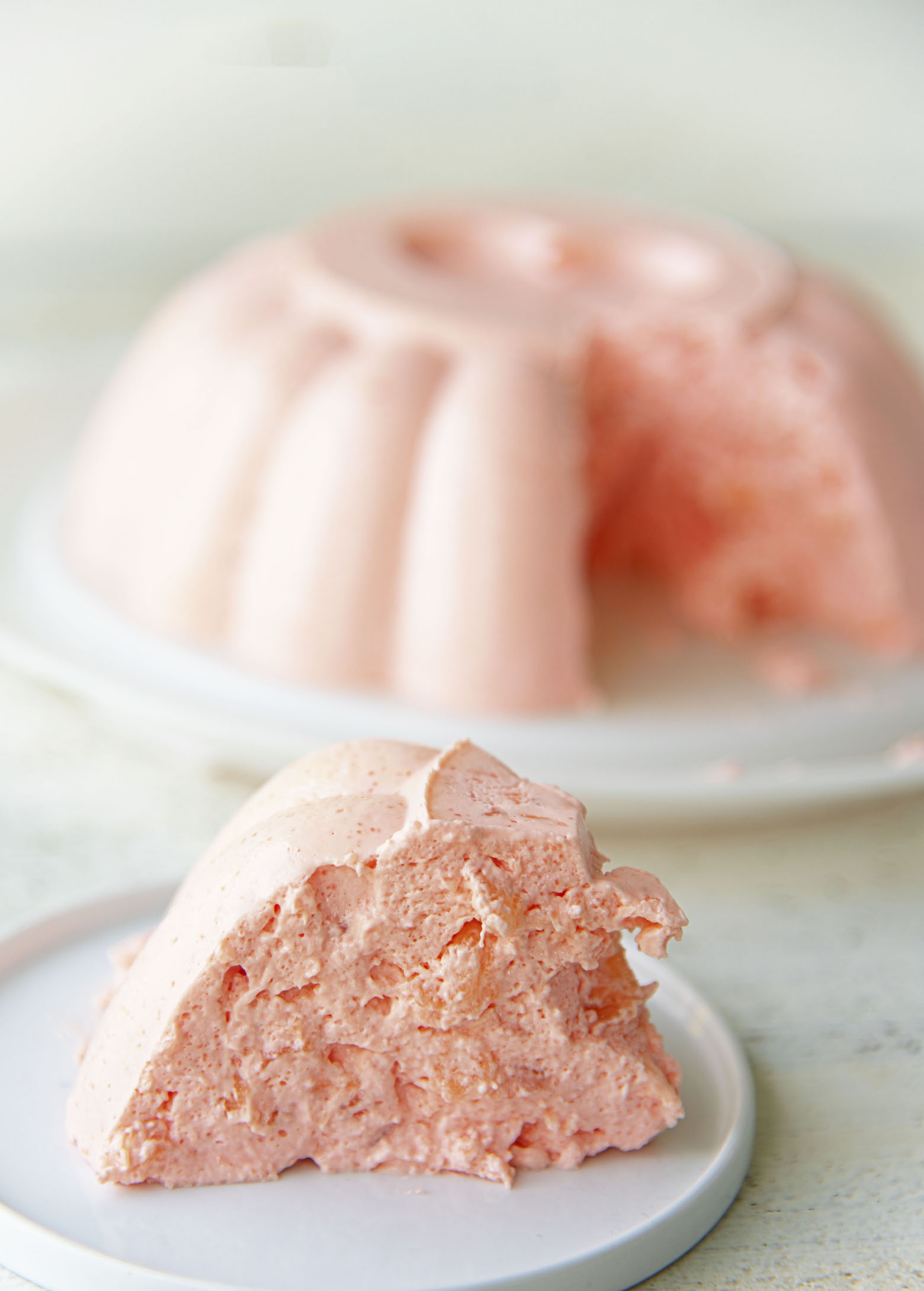 Slice of jello mold on a plate with remaining mold in the background. 