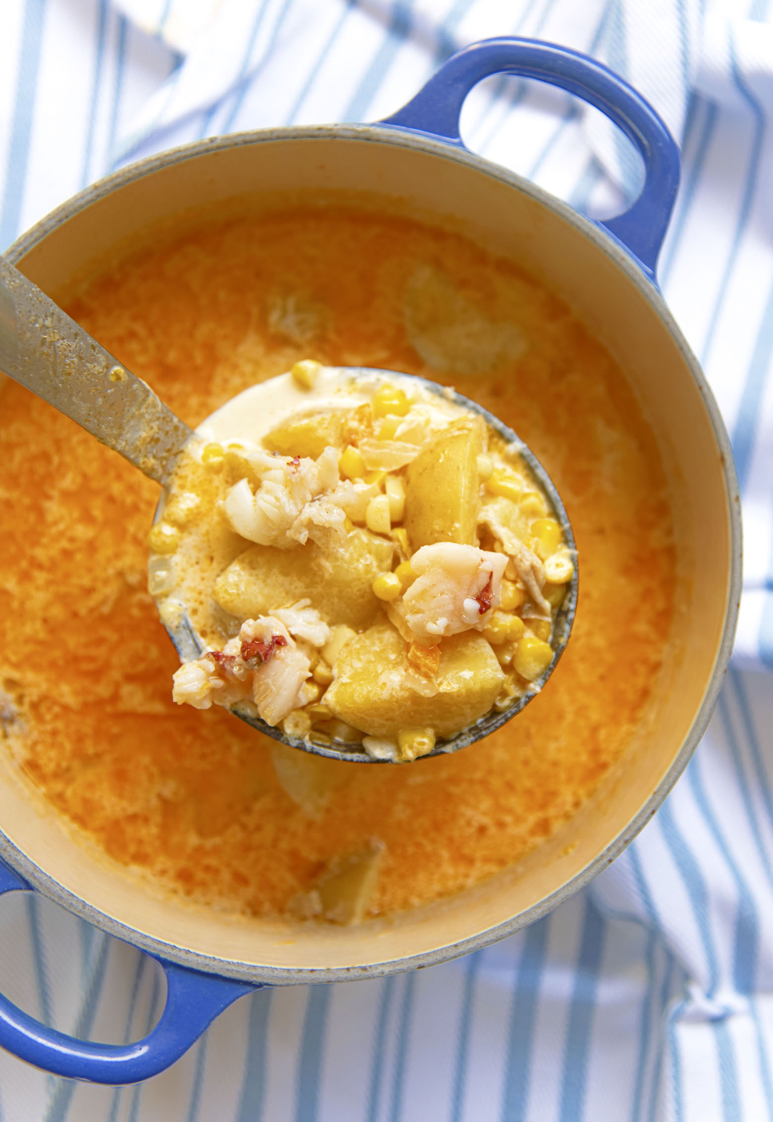 Overhead shot of a pot of Lobster Sweet Corn Chowder with an up close shot of the ingredients in the ladle. 