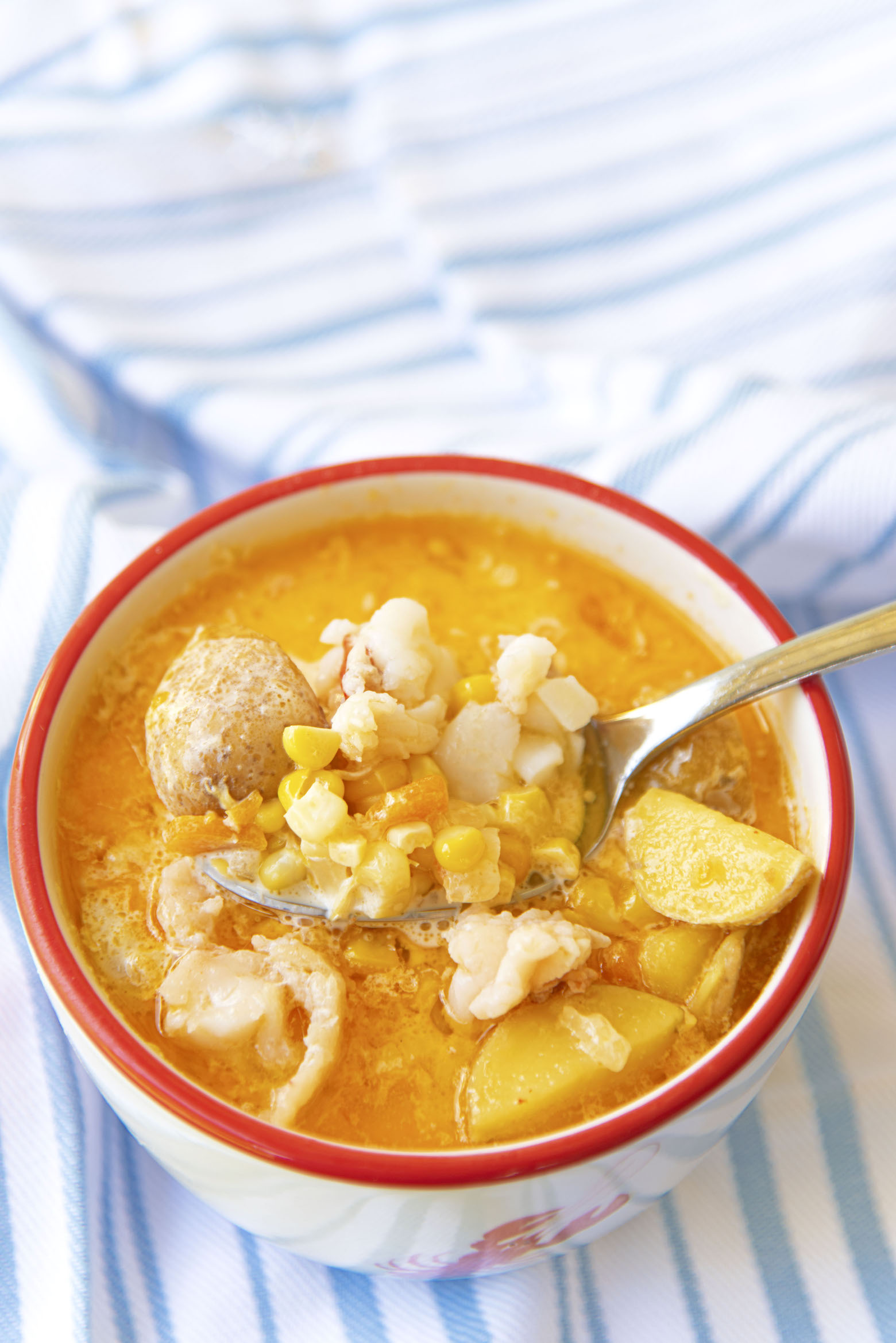 Bowl of chowder with a spoon coming up filled with corn, potatoes, and lobster.