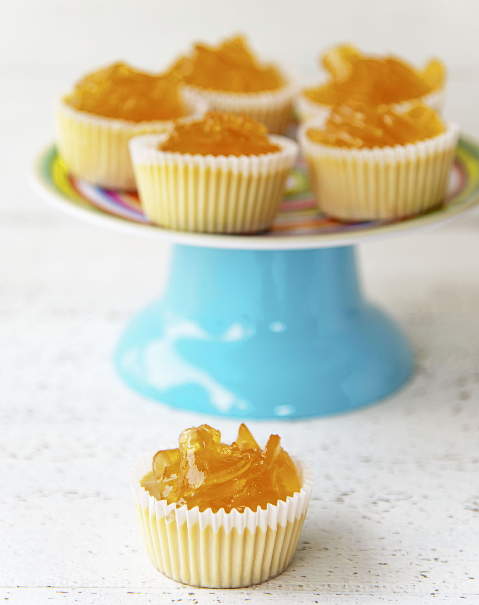 Side view of the cheesecake bites on a cake stand (in background) with a single cheesecake bite up front.