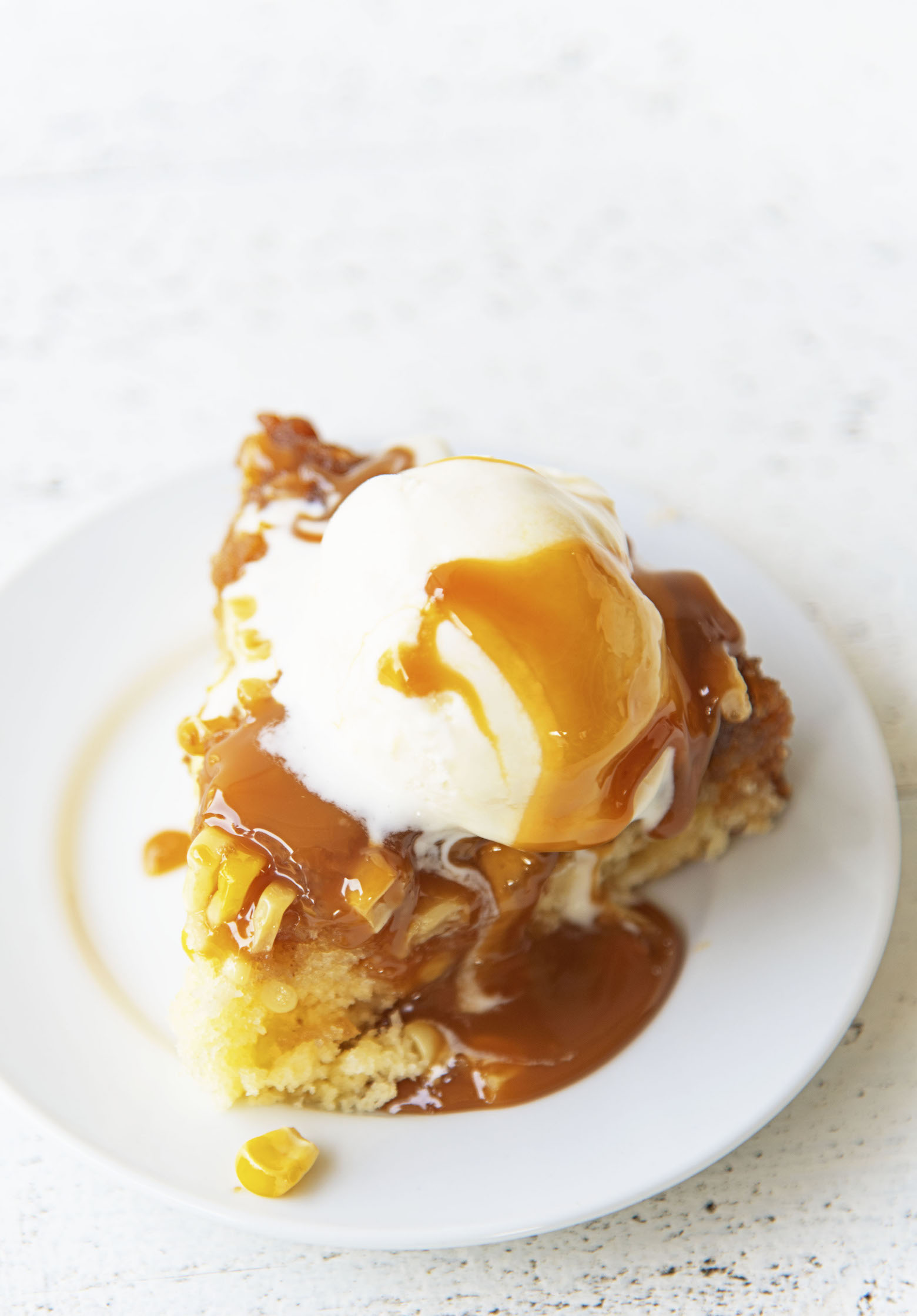 Three quarter shot of a single piece of upside down cake with ice cream and caramel sauce.